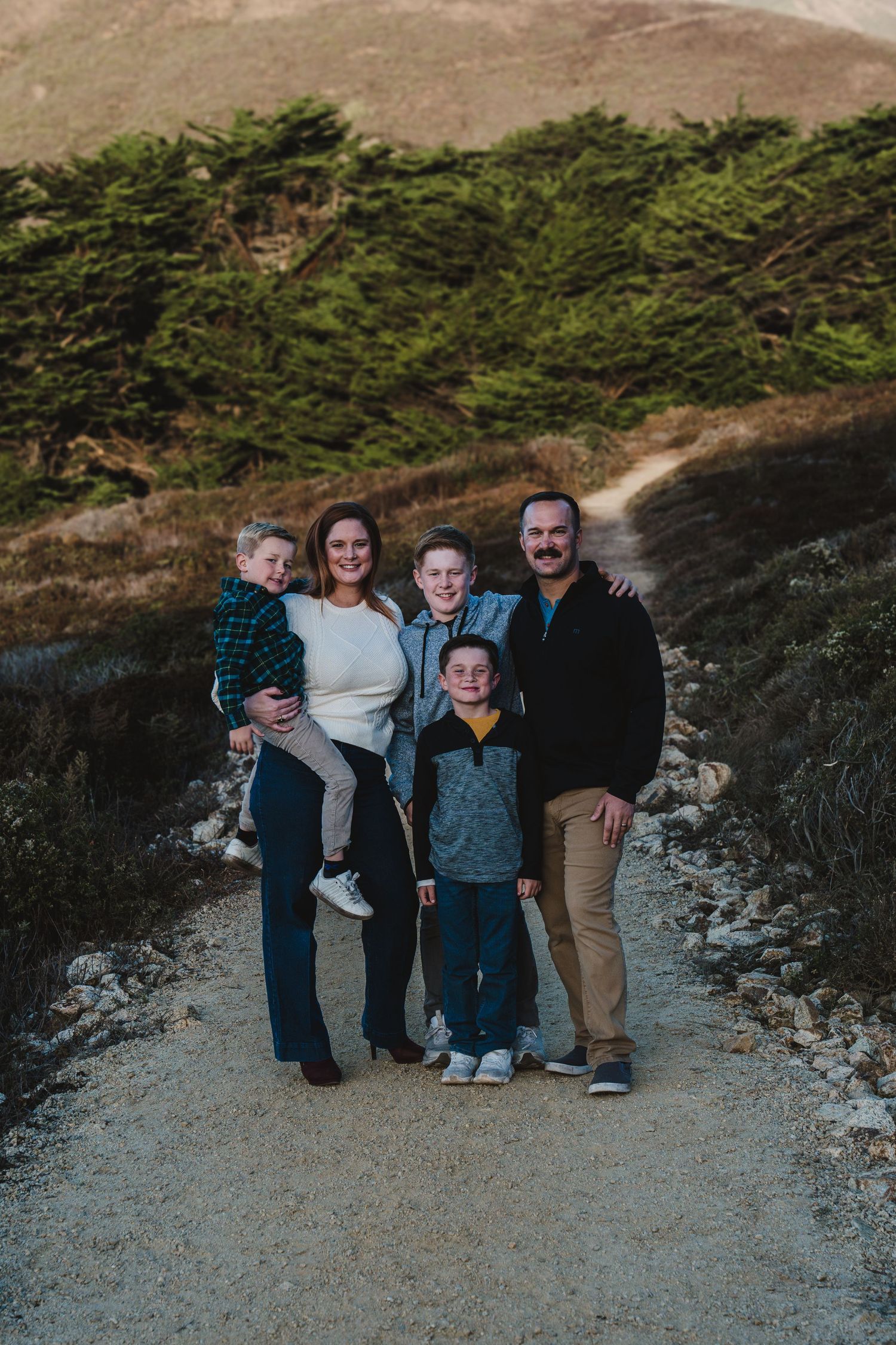 A group of people standing together on a coastal path with evergreen trees in the background at dusk in Big Sur.