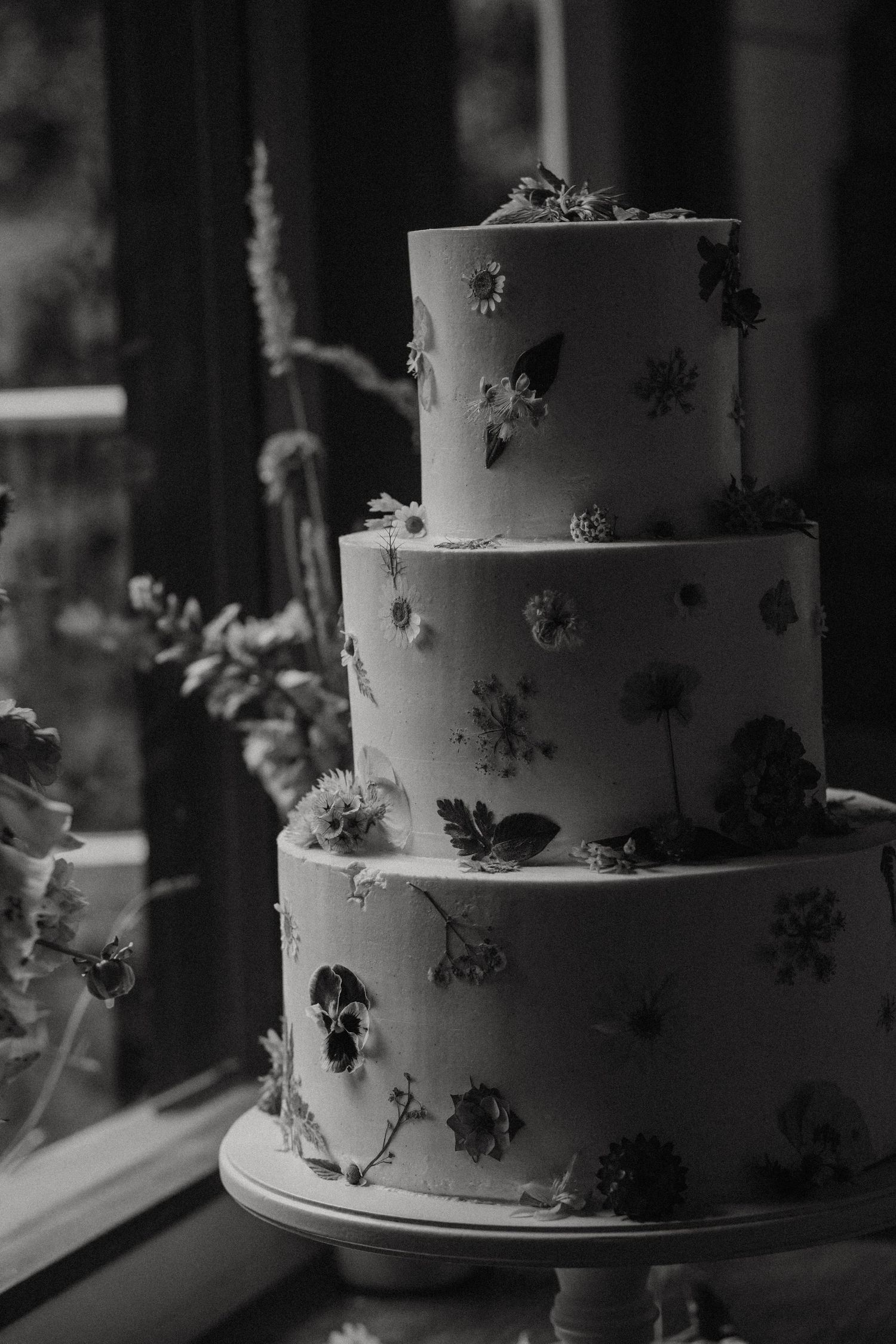 A black and white series of elegant tiered wedding cakes decorated with delicate floral details next to a window.