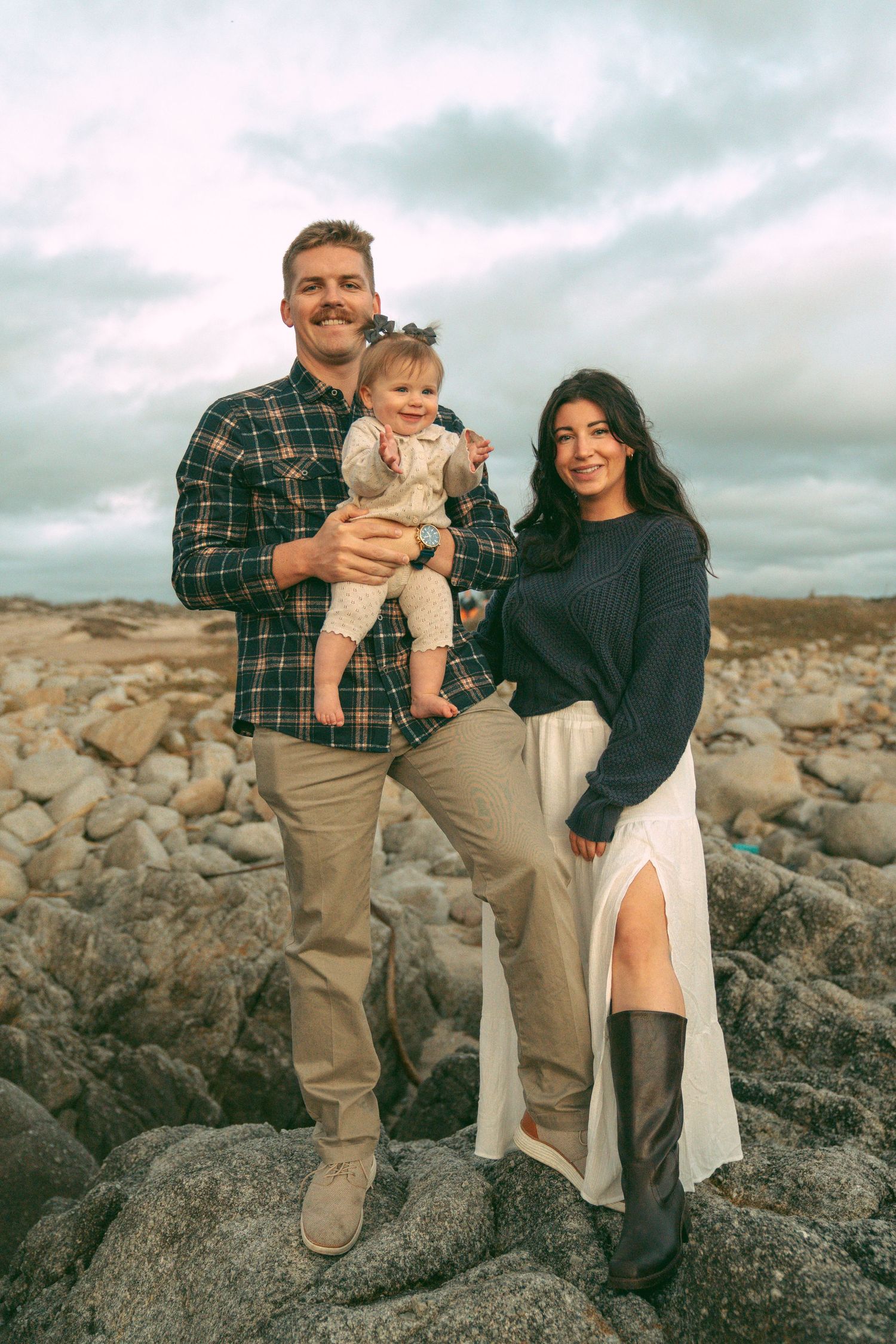 Family photos at Asilomar State Beach on rugged rock formations near the coastline under cloudy skies.