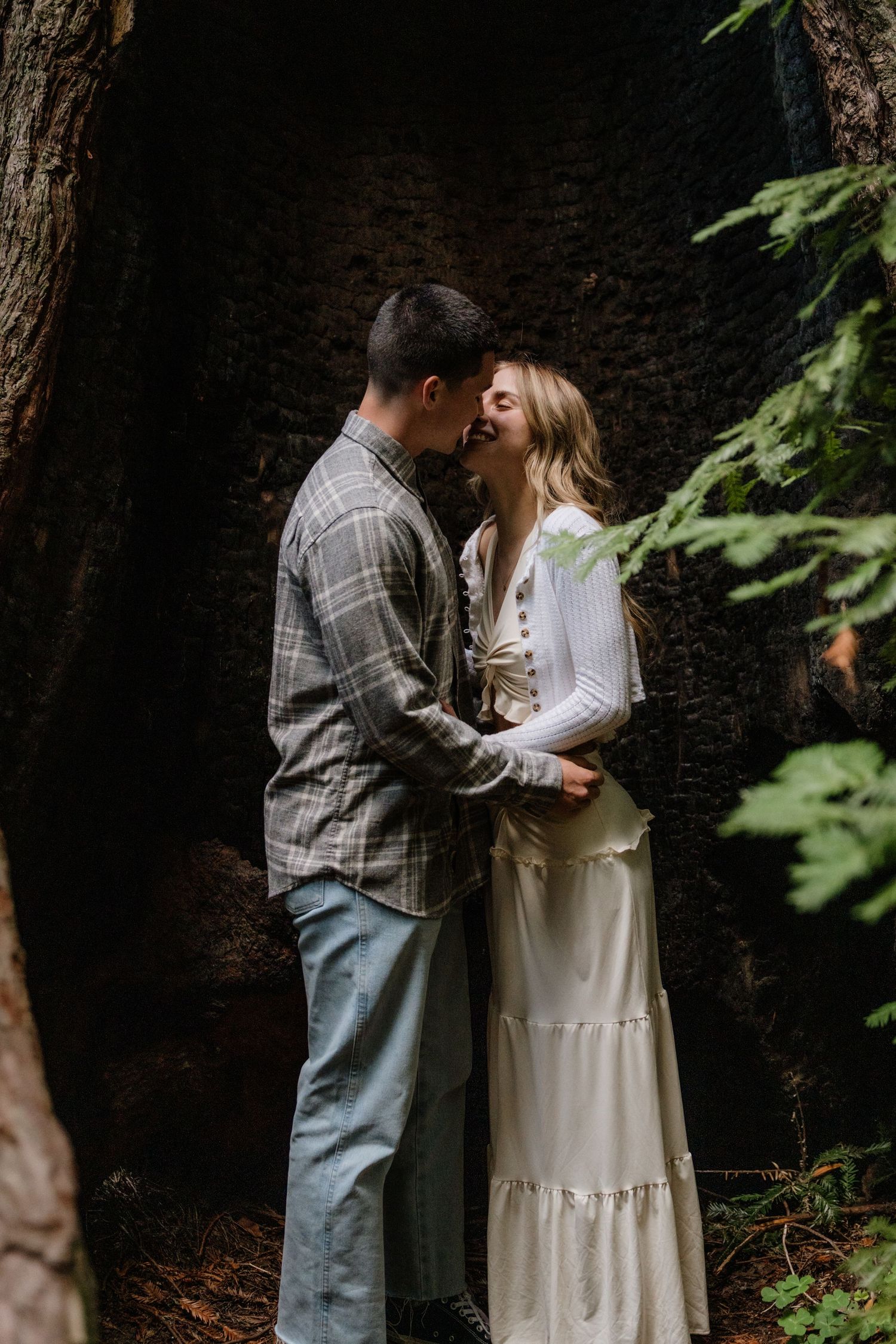 A loving couple shares an intimate moment in a wooded forest setting, with her wearing a flowy white dress and him in plaid in Big Sur .