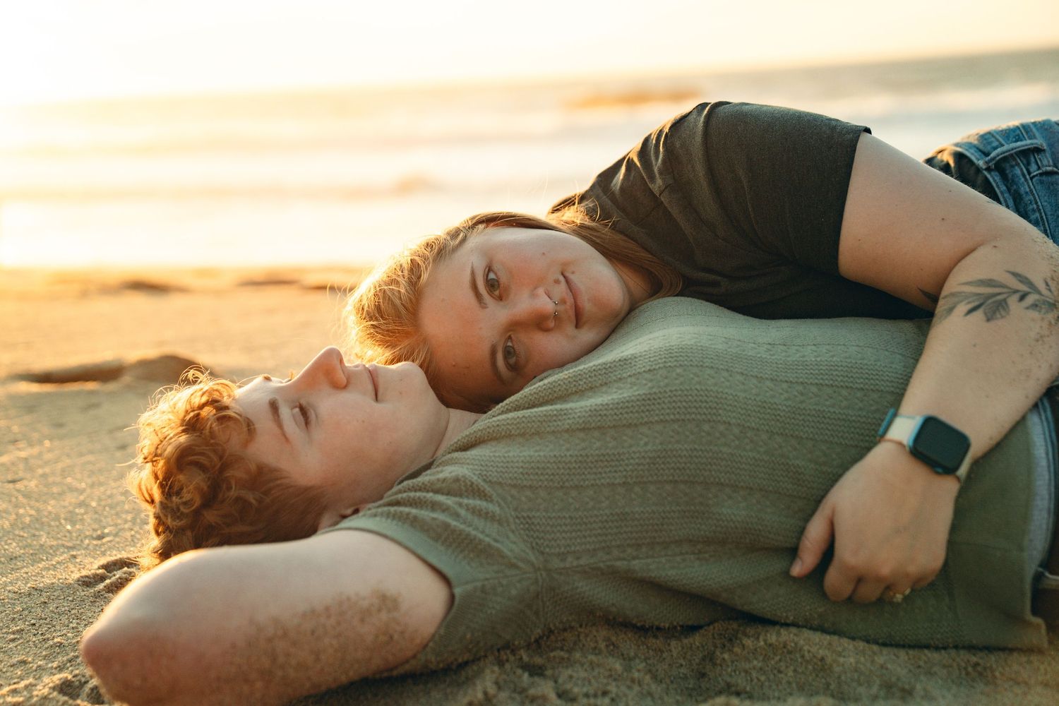 Two people lying on beach at sunset with soft golden light.