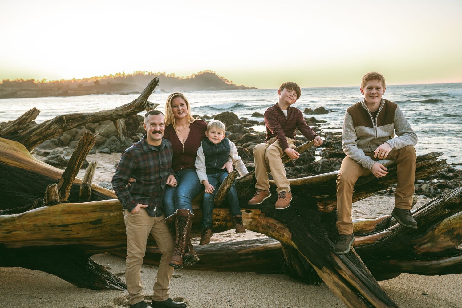 Group relaxing on driftwood logs at a scenic beach during sunset.