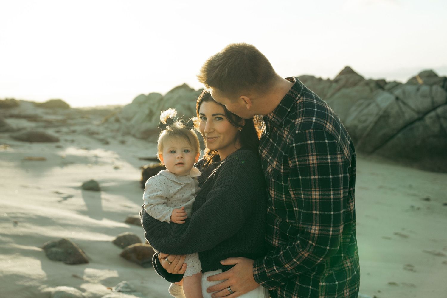 A parent and child share tender moments together on a misty beach with rocky cliffs in the background.