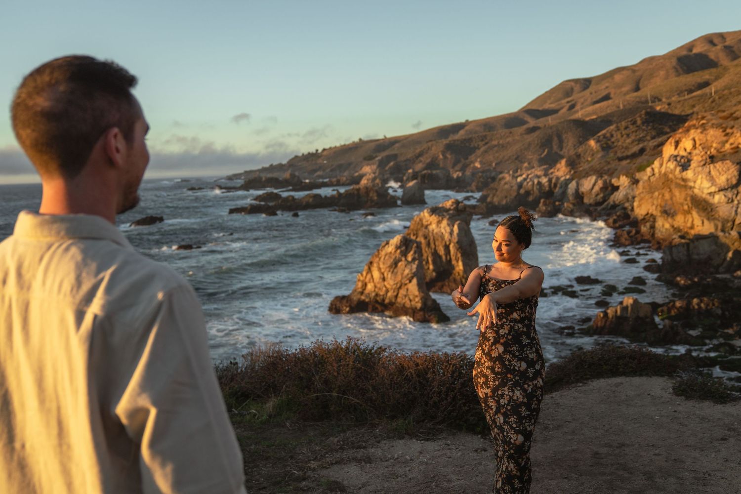 People walk along a scenic coastal trail with rugged cliffs and crashing waves at sunset in California.
