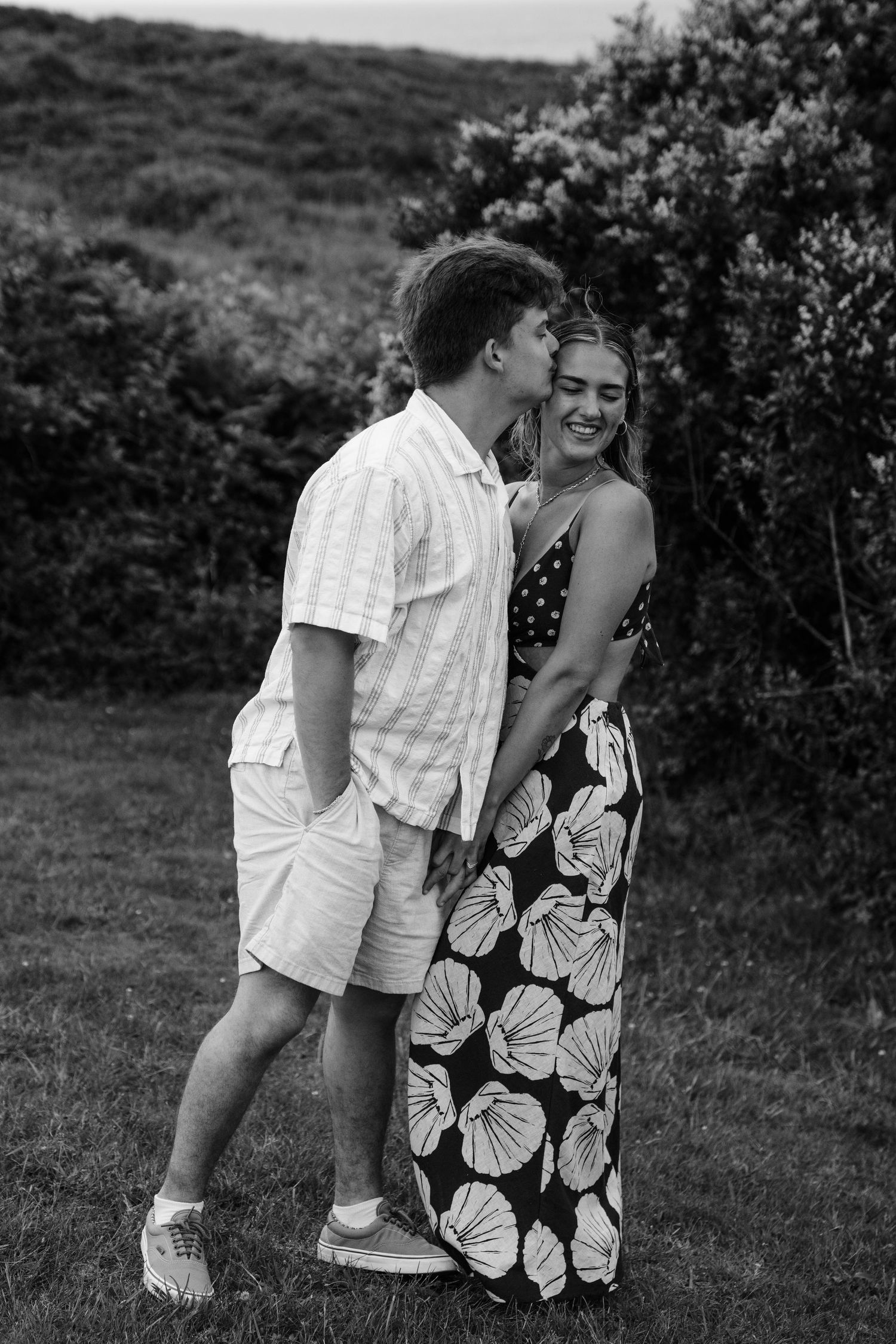A couple shares playful and romantic moments outdoors in black and white photography.