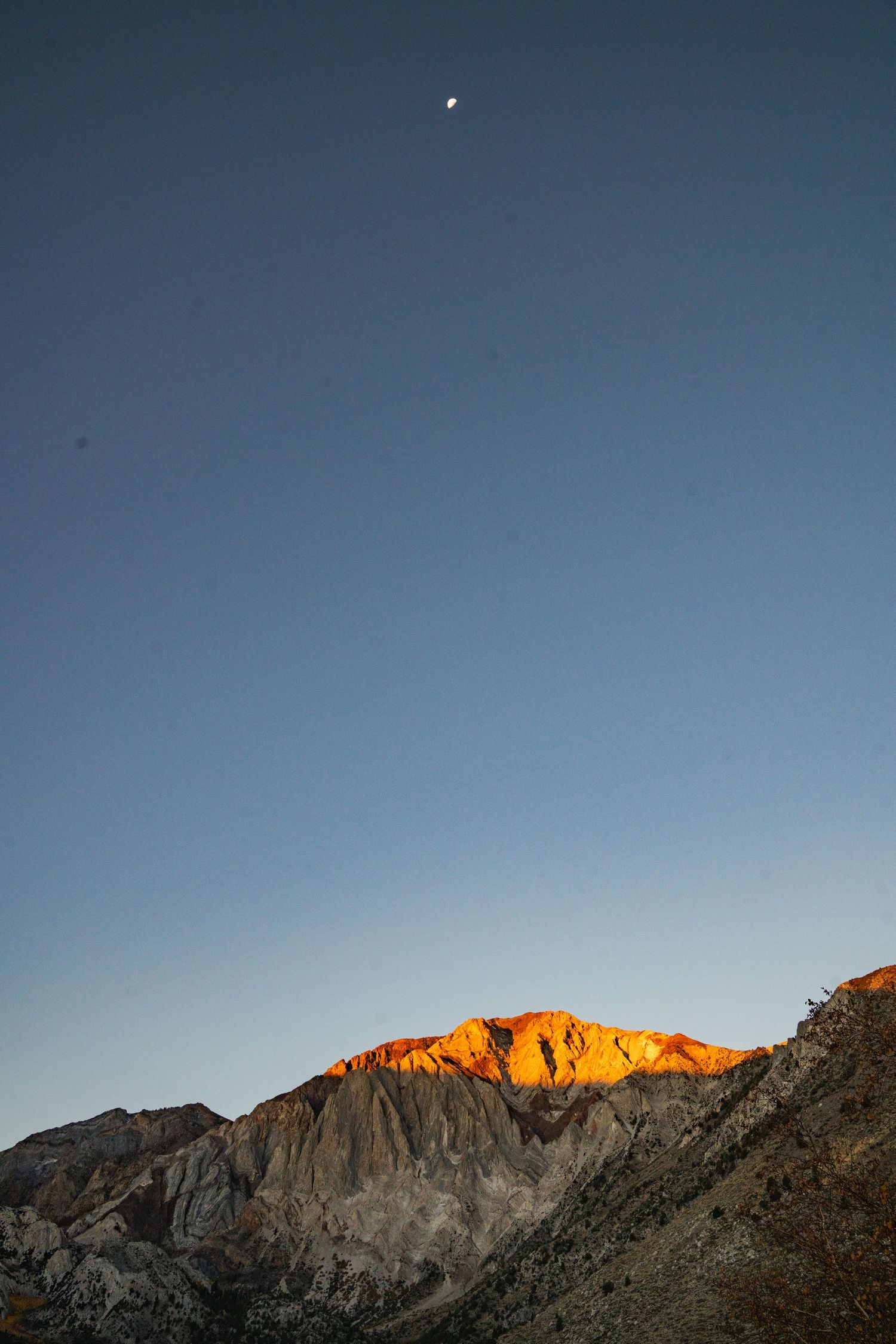 Rugged mountain peaks silhouetted against a clear blue sky with golden sunlight illuminating the highest ridge at sunset.