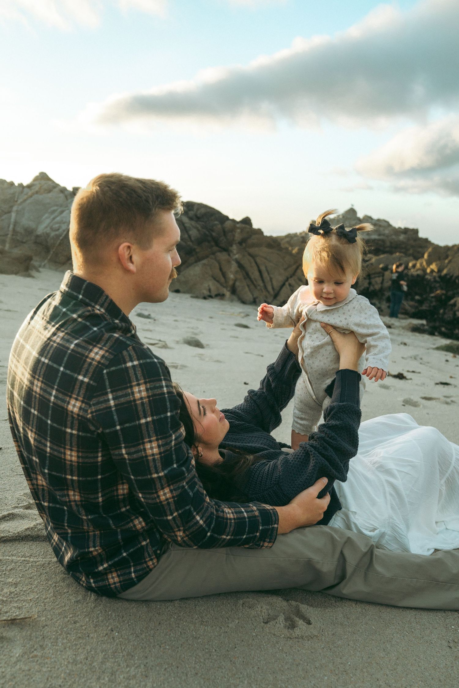Family enjoying quality time together on a rocky beach during sunset with dramatic coastal scenery.