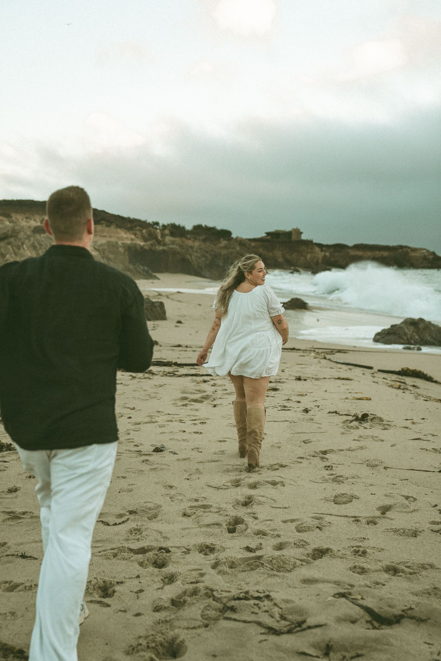 A couple walks along a misty coastal beach on an overcast day, capturing candid moments in multiple frames.