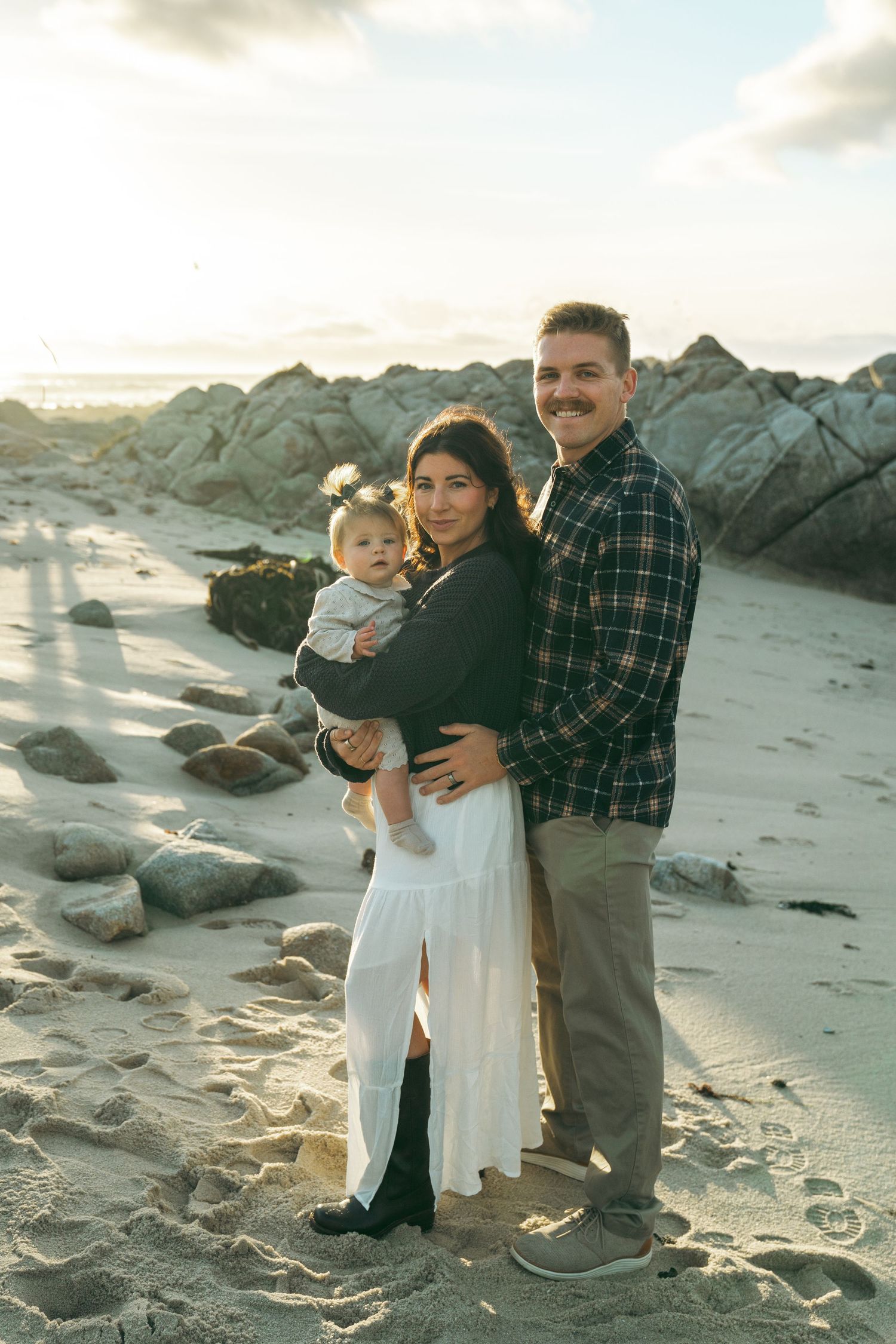 Family portrait on a beach with rocky outcrops during golden hour.