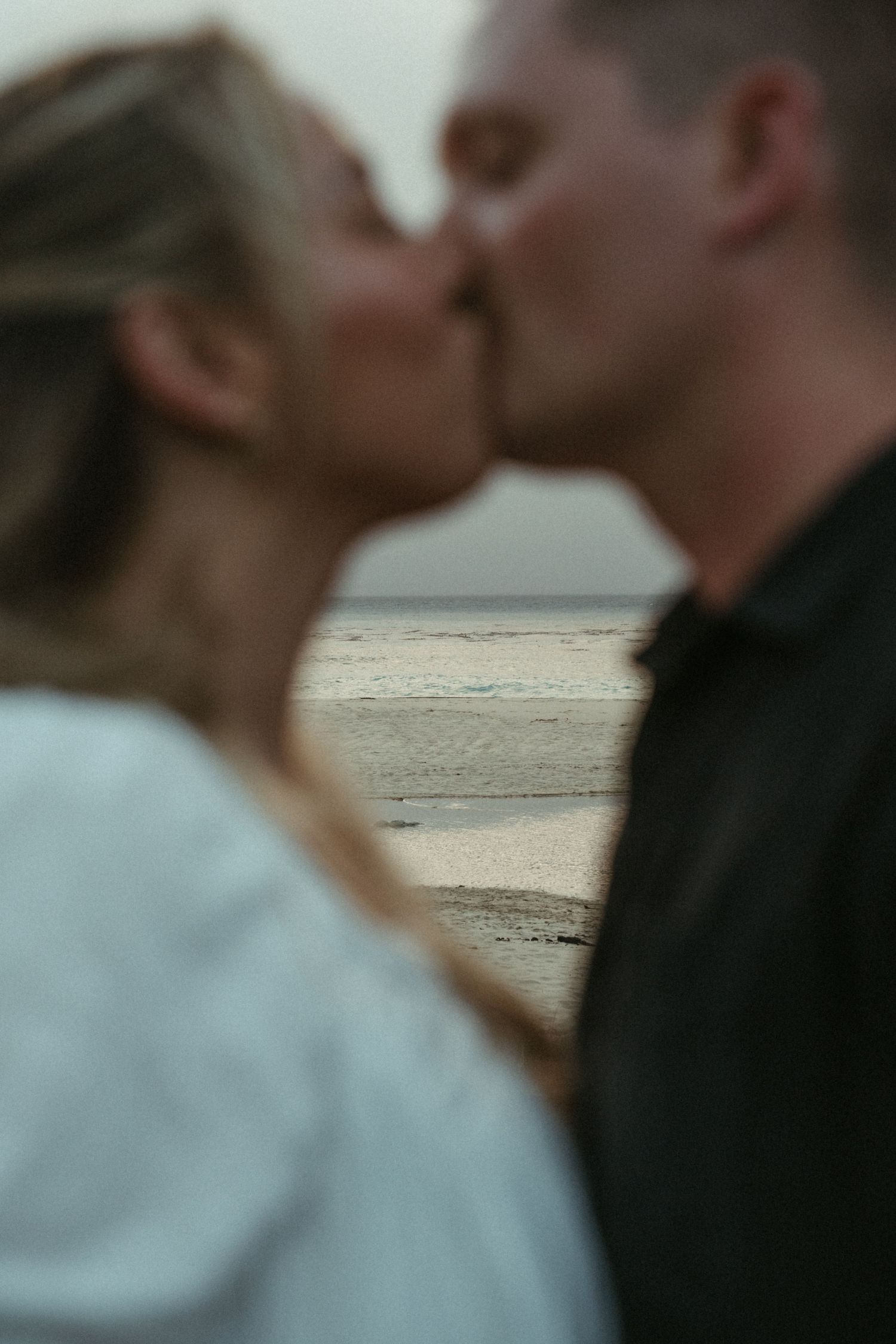 A romantic moment shared between a couple on the beach at dusk wearing contrasting white and black outfits.