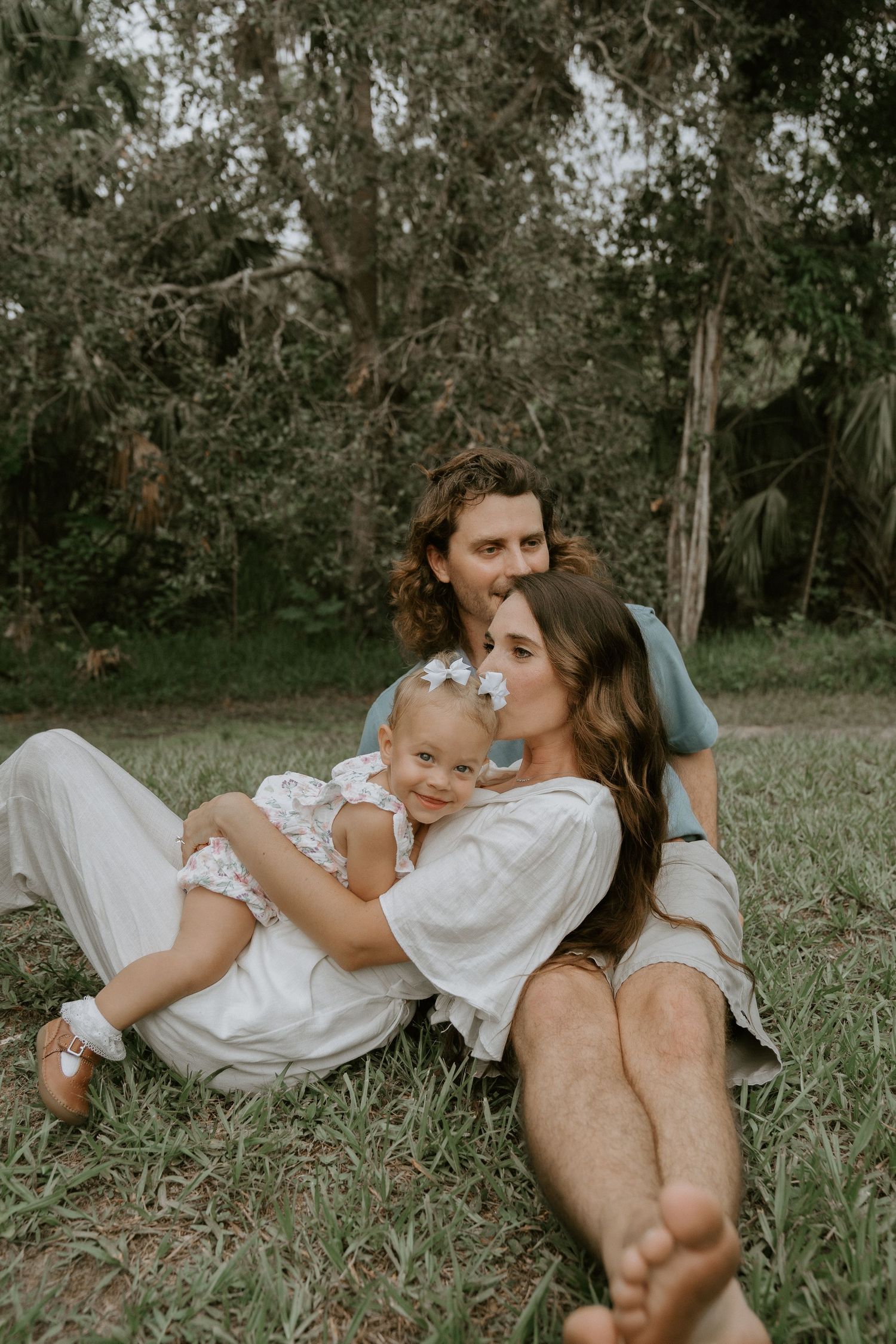 A tender family moment relaxing together on green grass under trees.