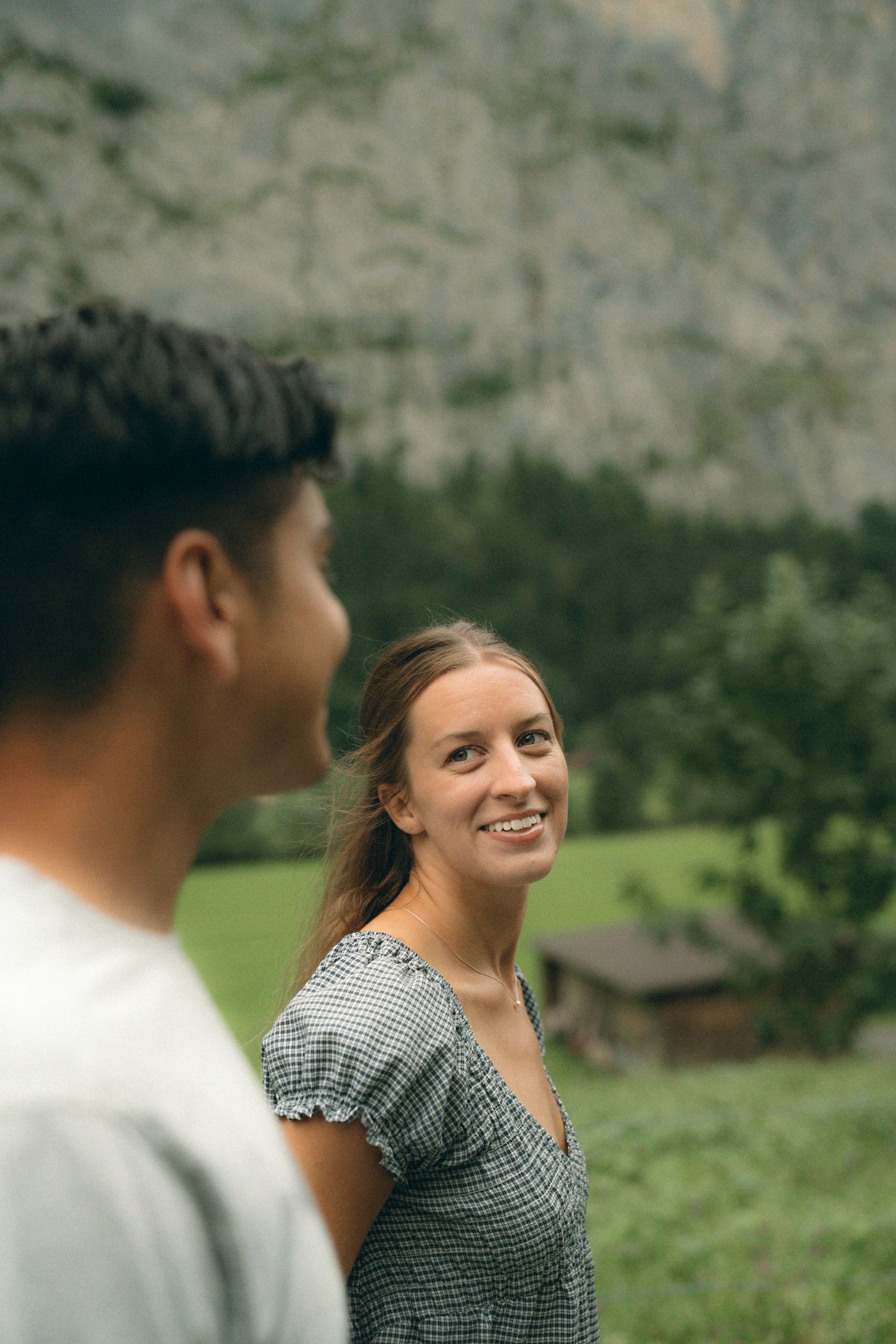 Two people share a joyful moment together in a scenic mountain meadow setting with dramatic cliffs in the background.