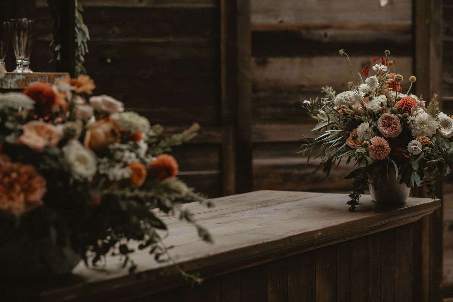 Rustic wood table decorated with blush and white floral arrangements and candlesticks against a moody dark background.