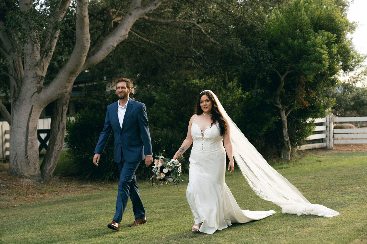 Couple walking together through a scenic outdoor garden path surrounded by lush trees.