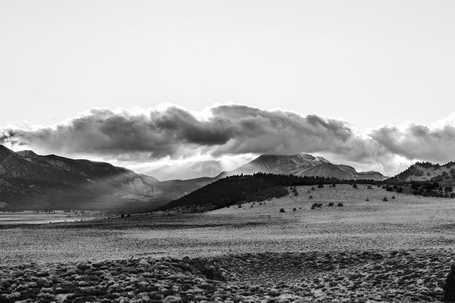 Dramatic black and white landscape of rolling hills and mountains with dark storm clouds gathering overhead.