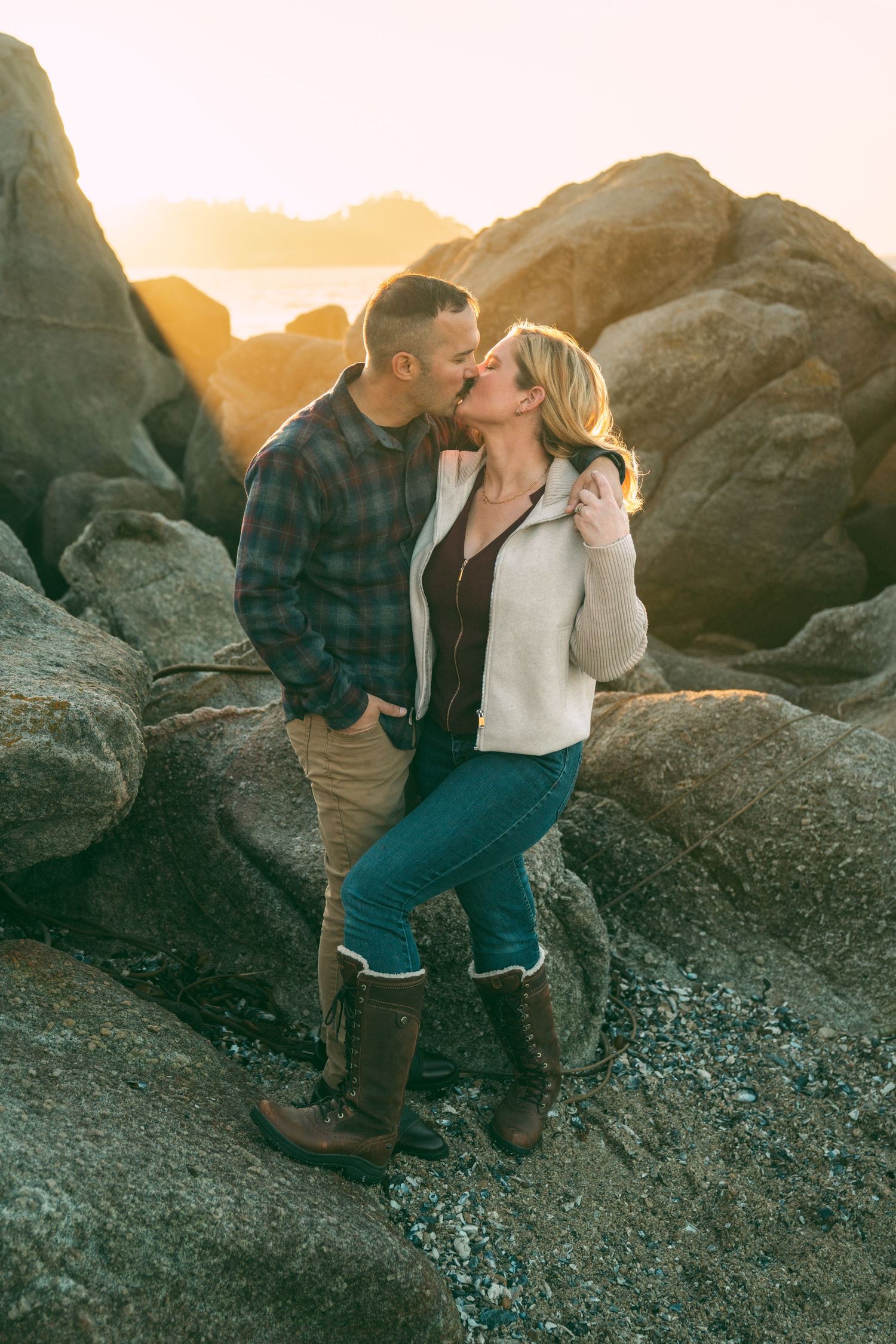 A romantic couple shares intimate moments on coastal rocks during golden hour sunset.