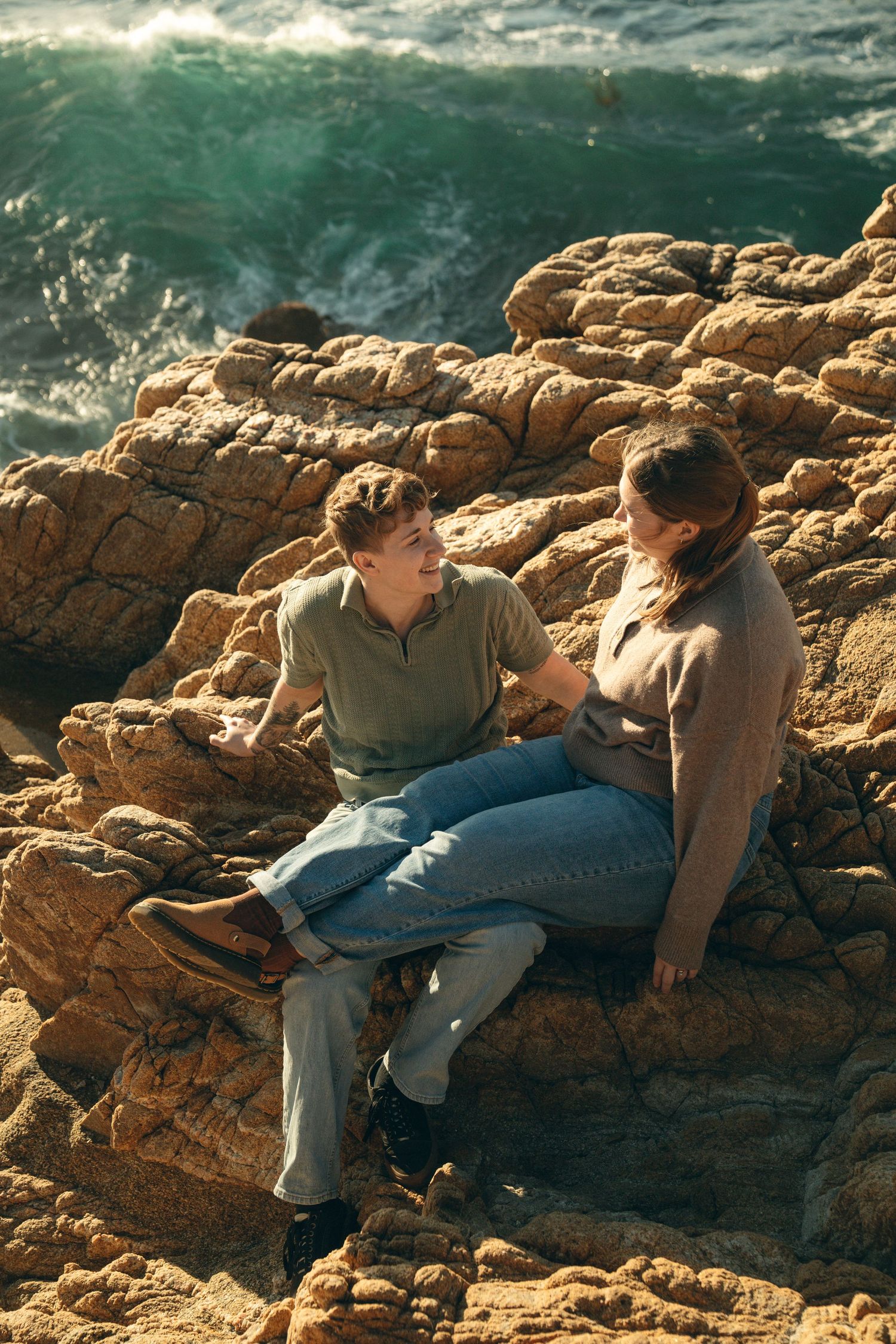 Couple sharing an intimate moment on coastal rocks with ocean waves in background.