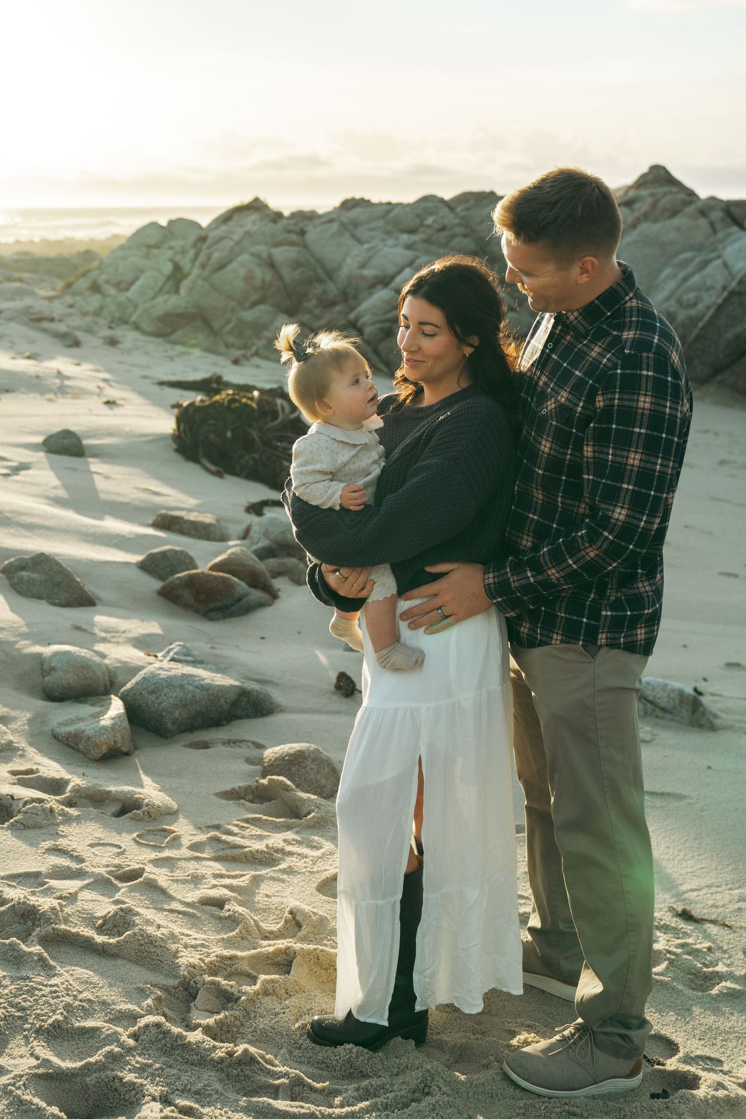 A family shares tender moments together while standing on a rocky beach at sunset.