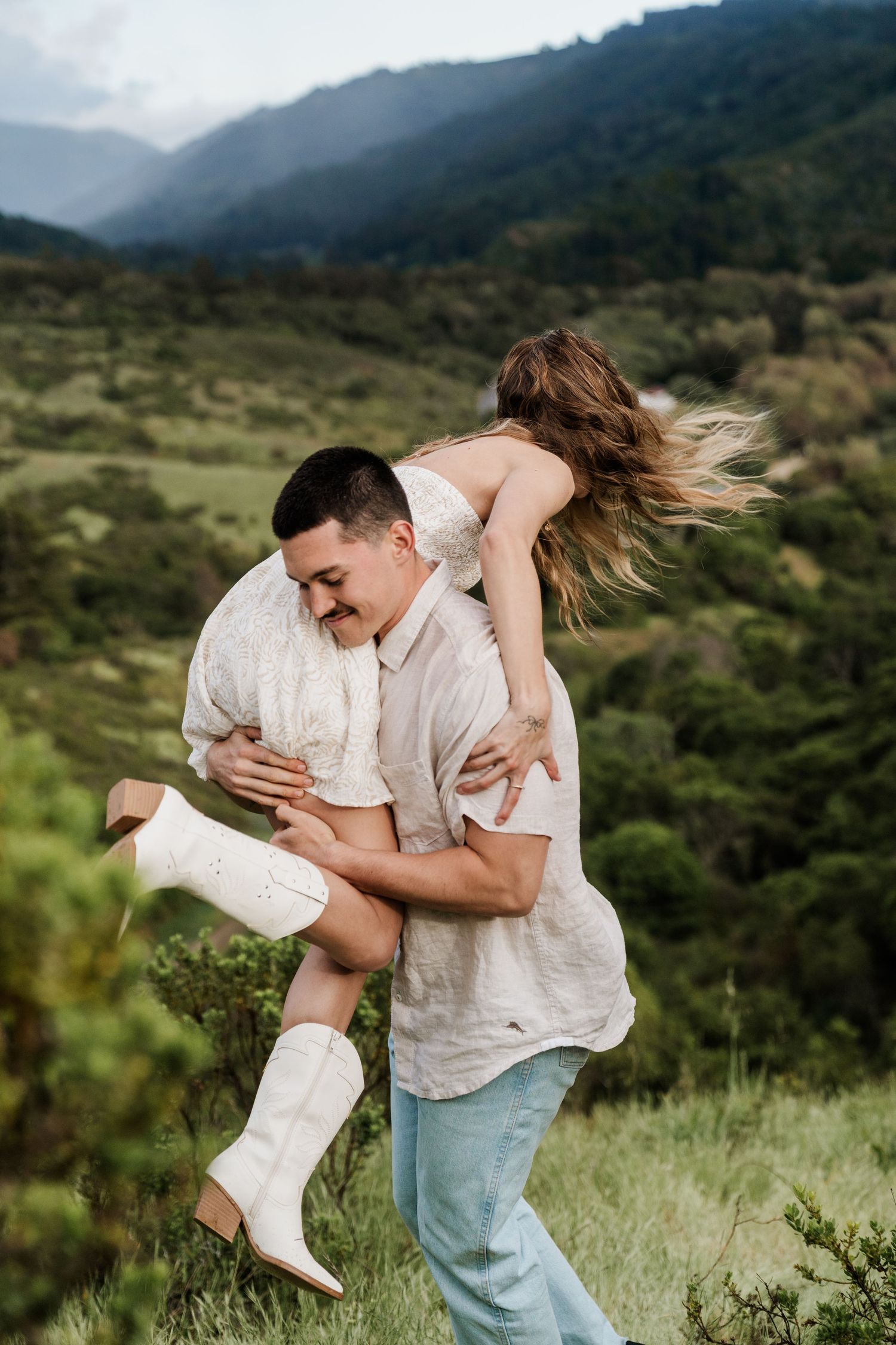 A couple plays and laughs together in a green mountain meadow.