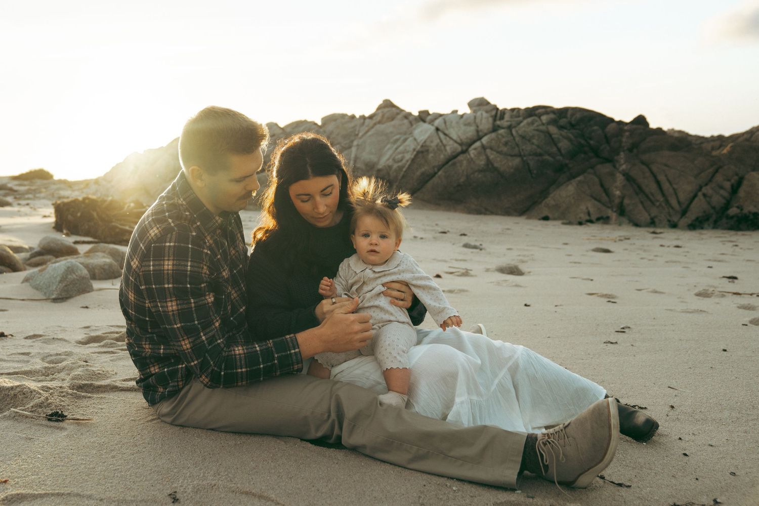 Family relaxing together on a rocky beach during golden hour wearing casual clothing.