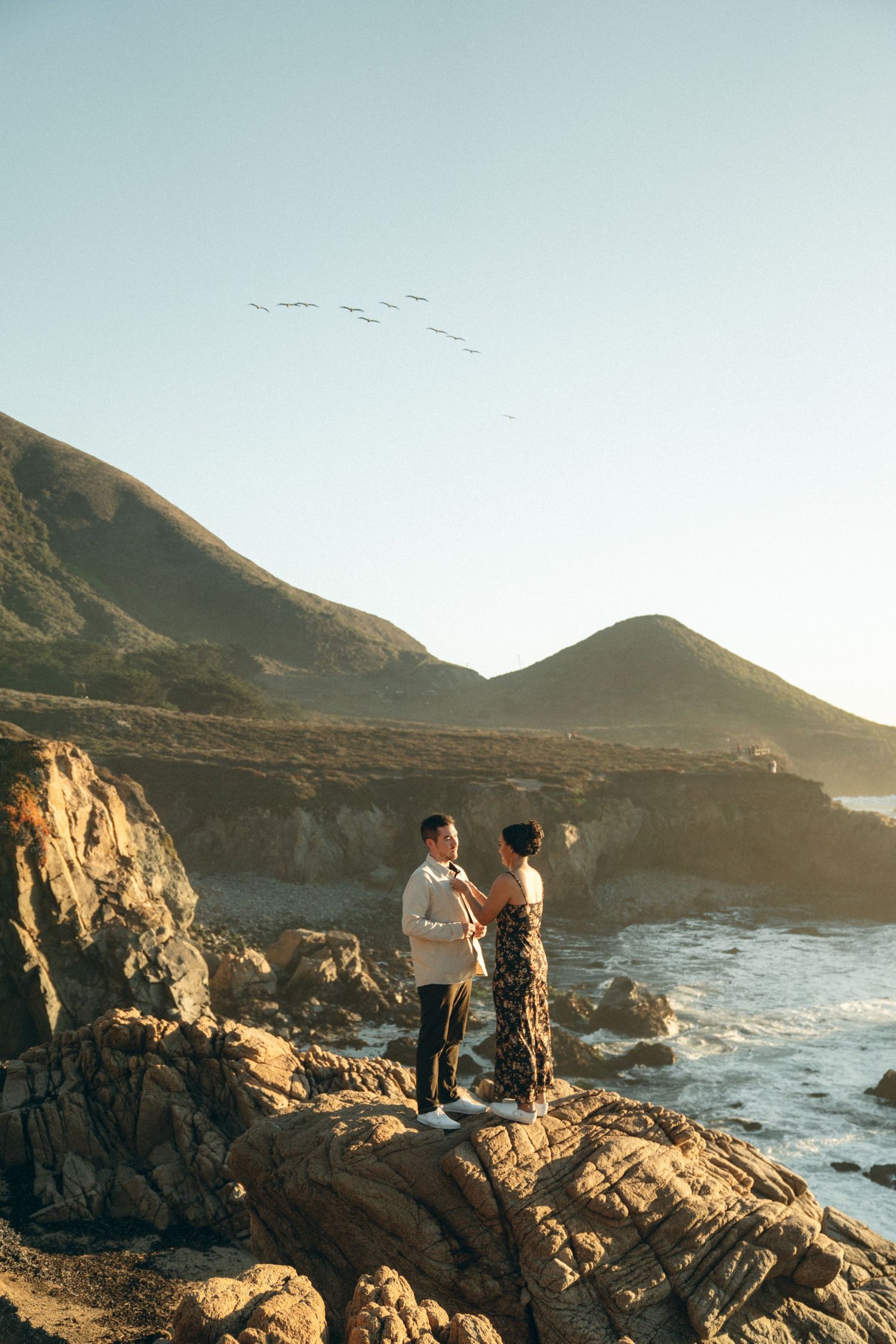 Couple enjoying sunset views of rugged coastal cliffs and crashing waves along Big Sur's dramatic Pacific coastline.