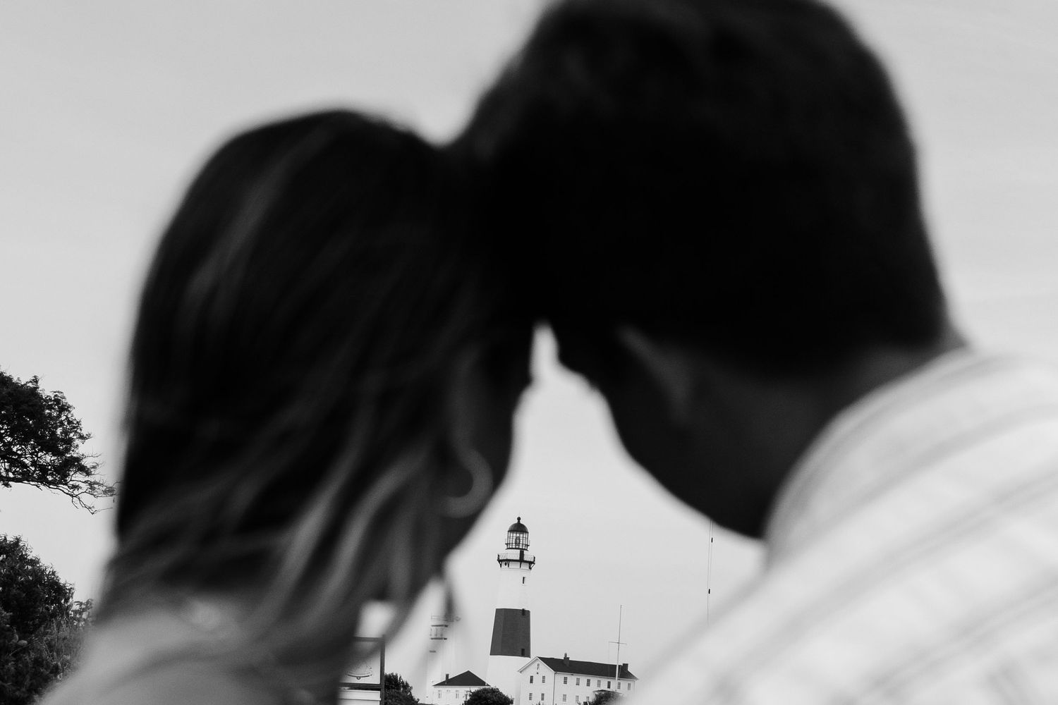 A silhouetted couple frames a white lighthouse in a black and white romantic composition.