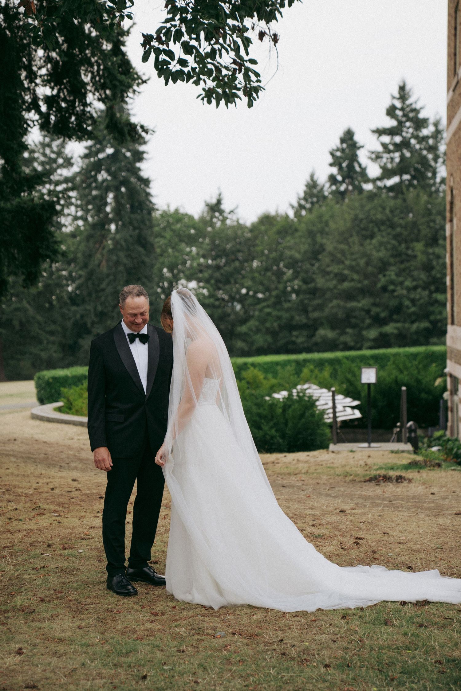 Candid wedding first look moments captured on grassy hillside with trees in background.