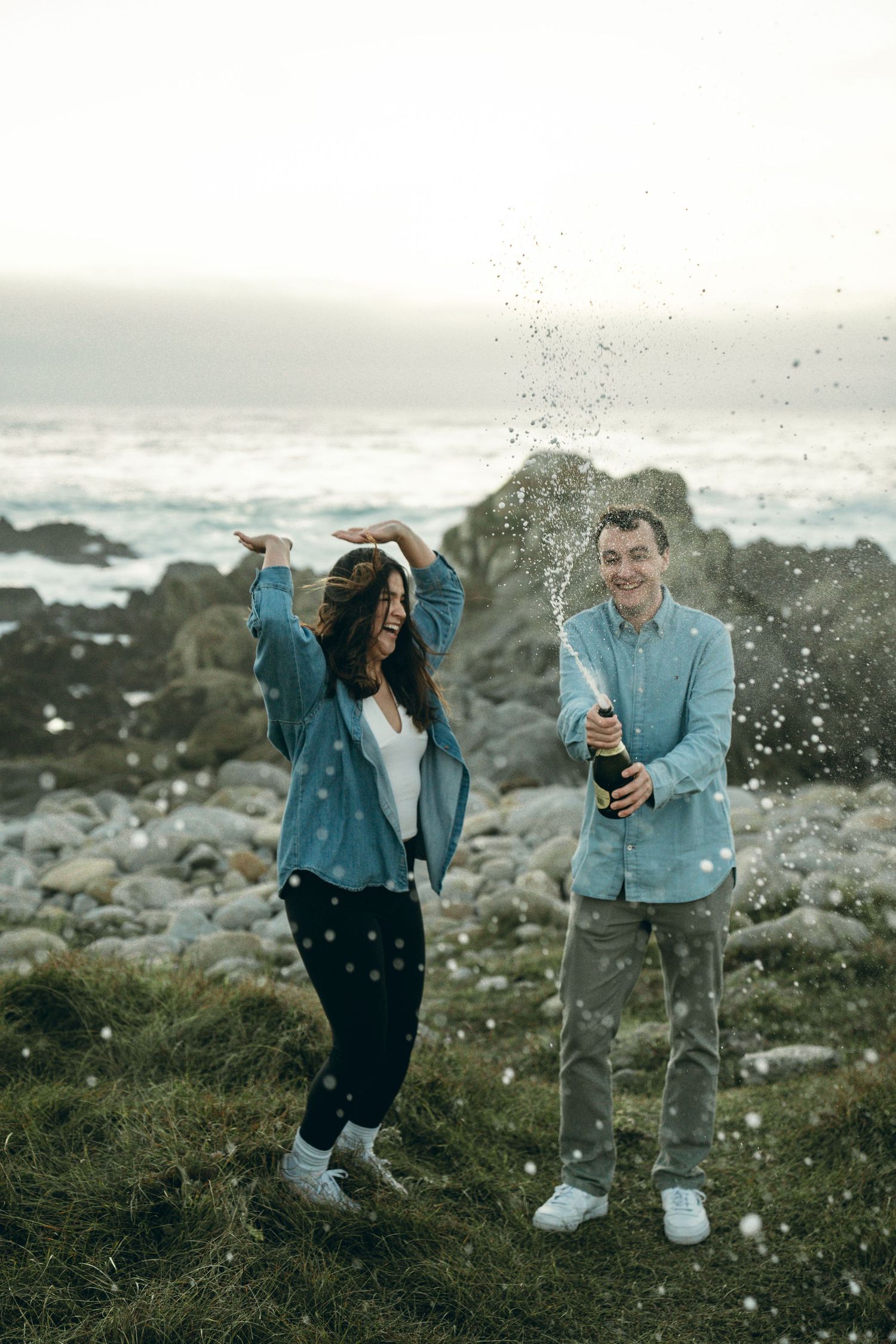 A playful moment captured on a rocky coastal cliff with ocean waves splashing in the background.