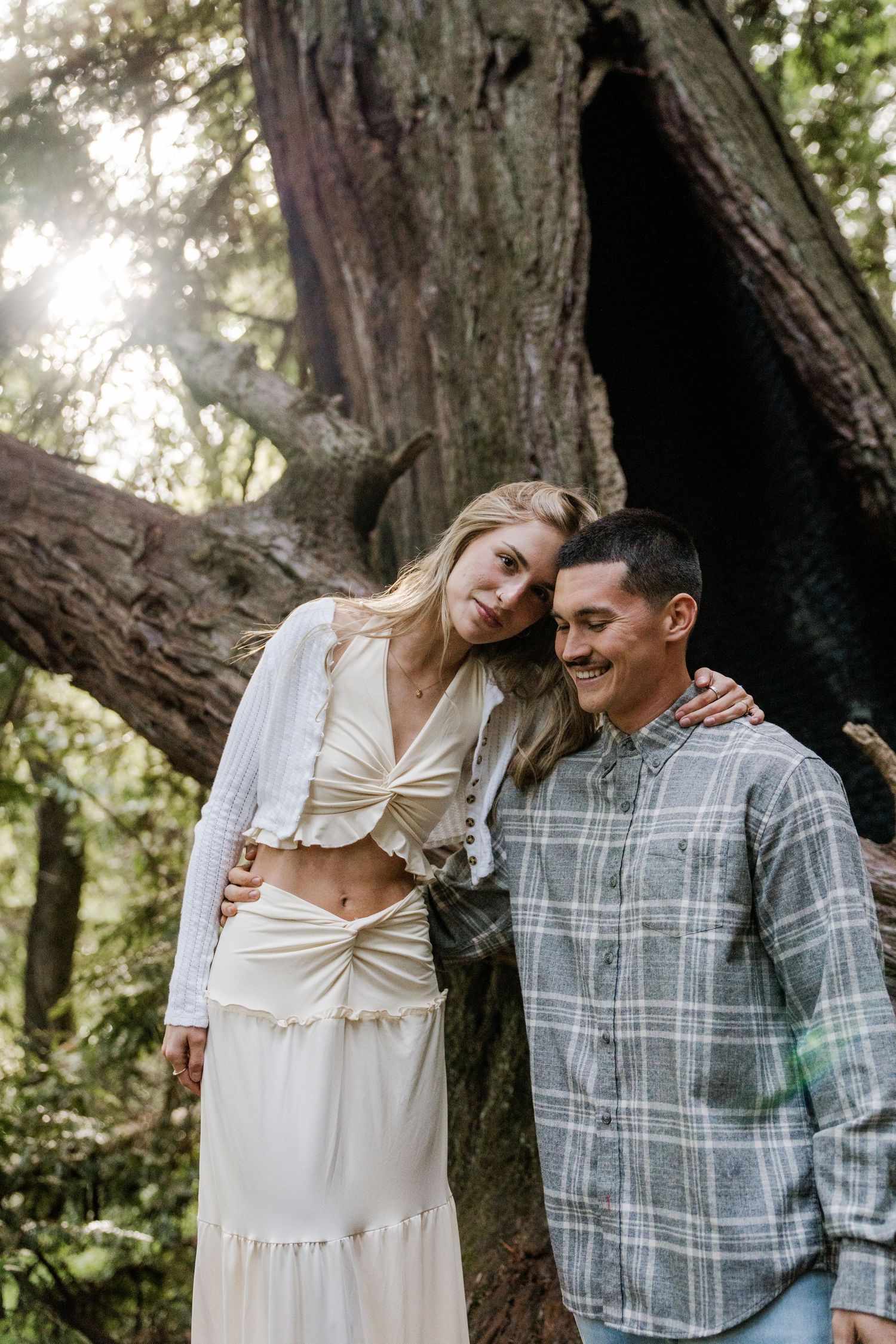 A couple enjoys a tender moment together against a backdrop of towering trees in a romantic forest setting in Big Sur California.