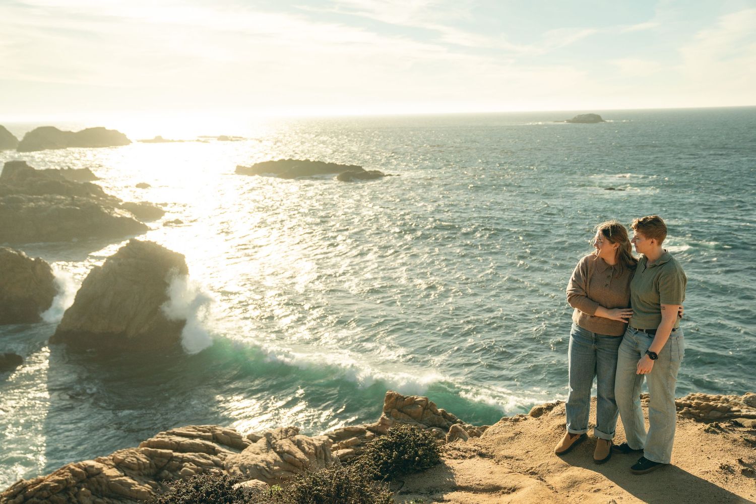 Scenic coastal landscape with two figures silhouetted against golden ocean sunset.