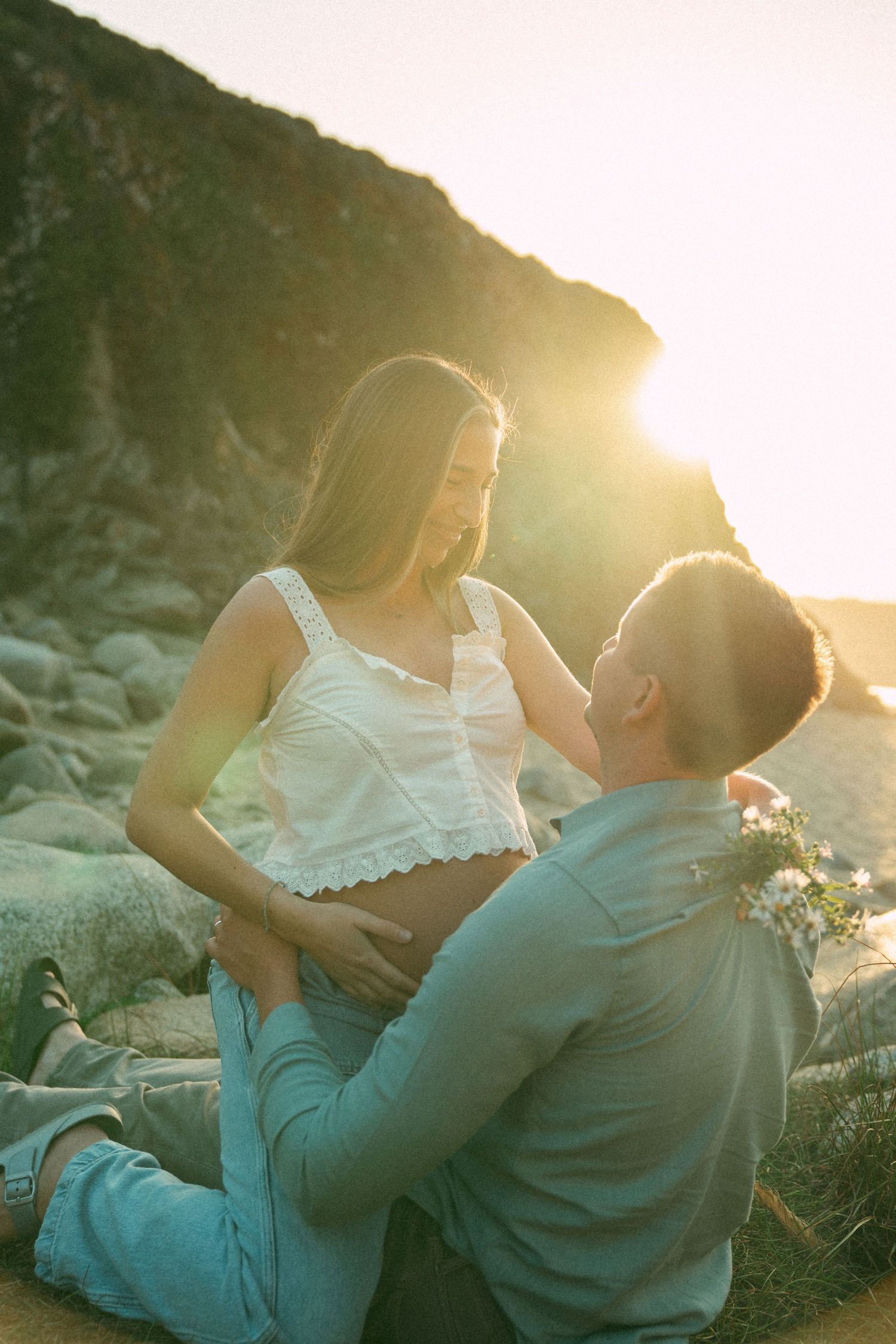 A couple sits together on rocky terrain during golden hour sunset, sharing intimate moments in a series of romantic poses.