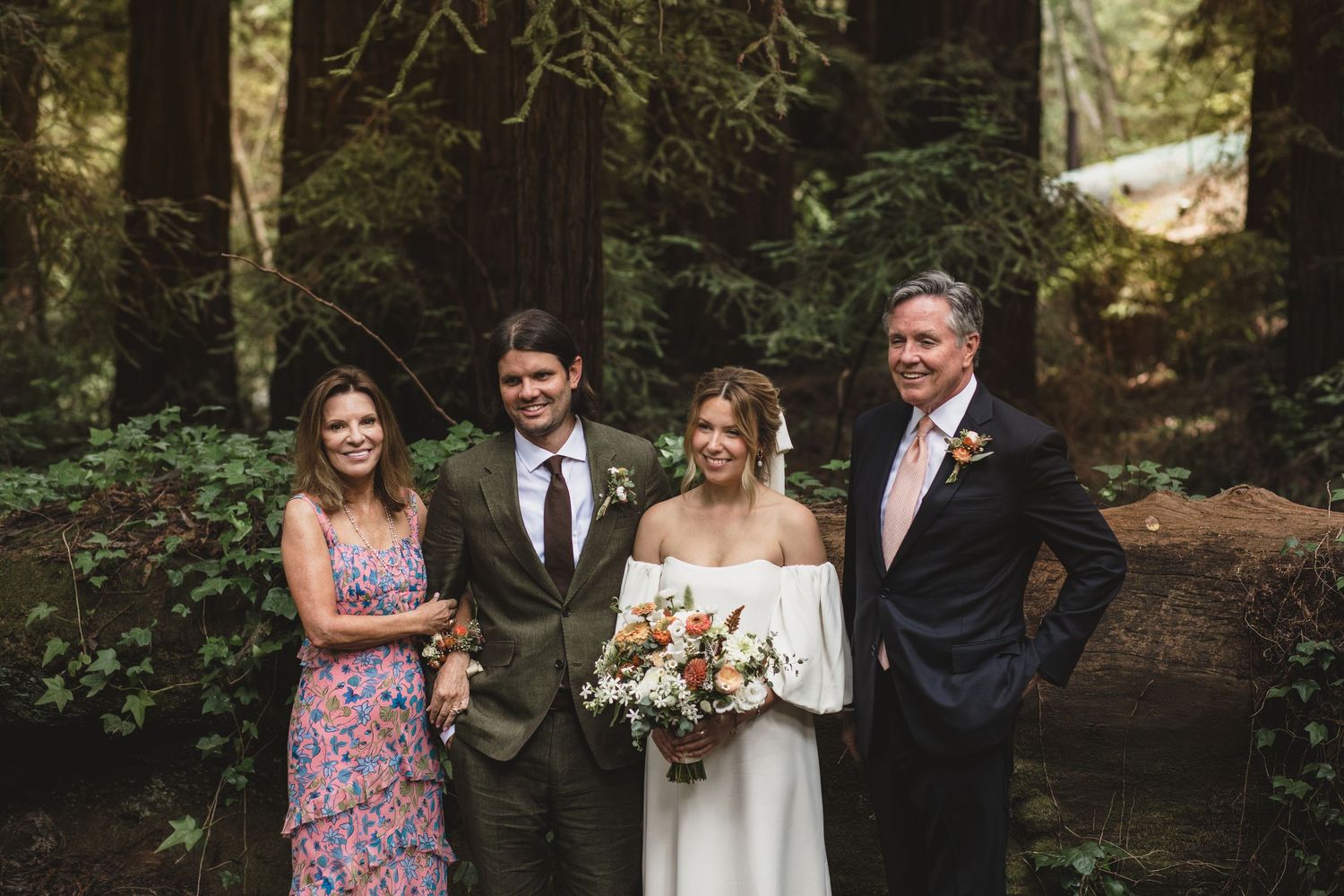 A wedding party stands together in a lush forest setting with greenery and trees in the background.