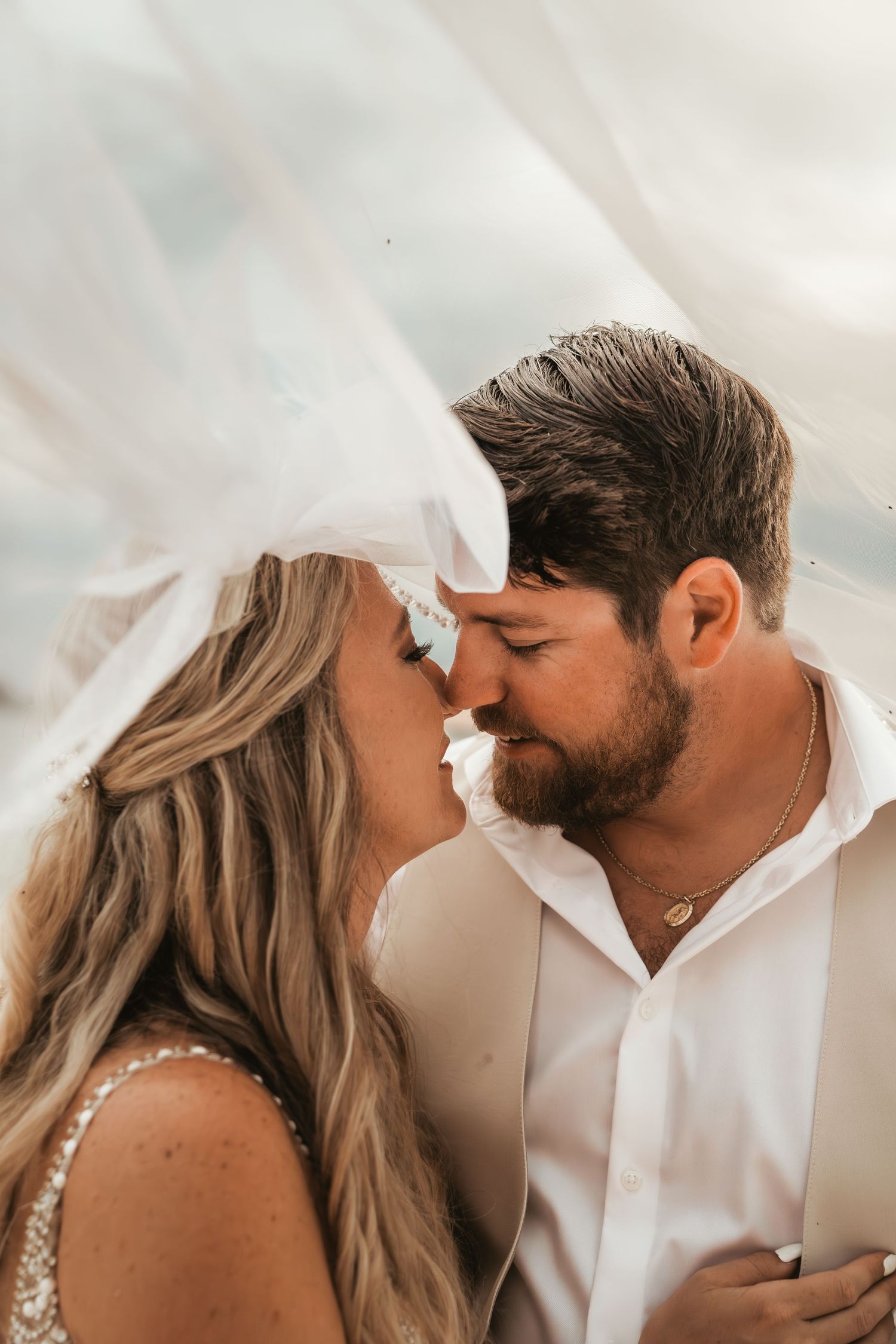 A couple shares an intimate moment during a romantic photoshoot against a light colored background.
