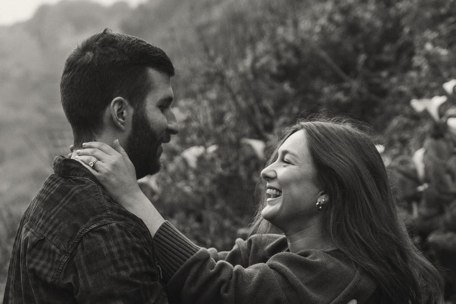 A black and white intimate portrait of a couple sharing a tender moment outdoors.