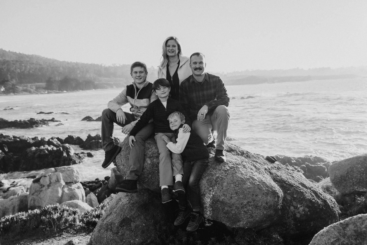 A group of people pose together on coastal rocks with ocean waves and scenic views in the background.