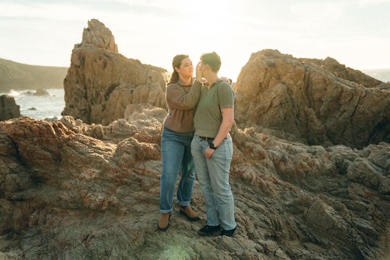 Couple walking together along rocky coastal cliffs at sunset.
