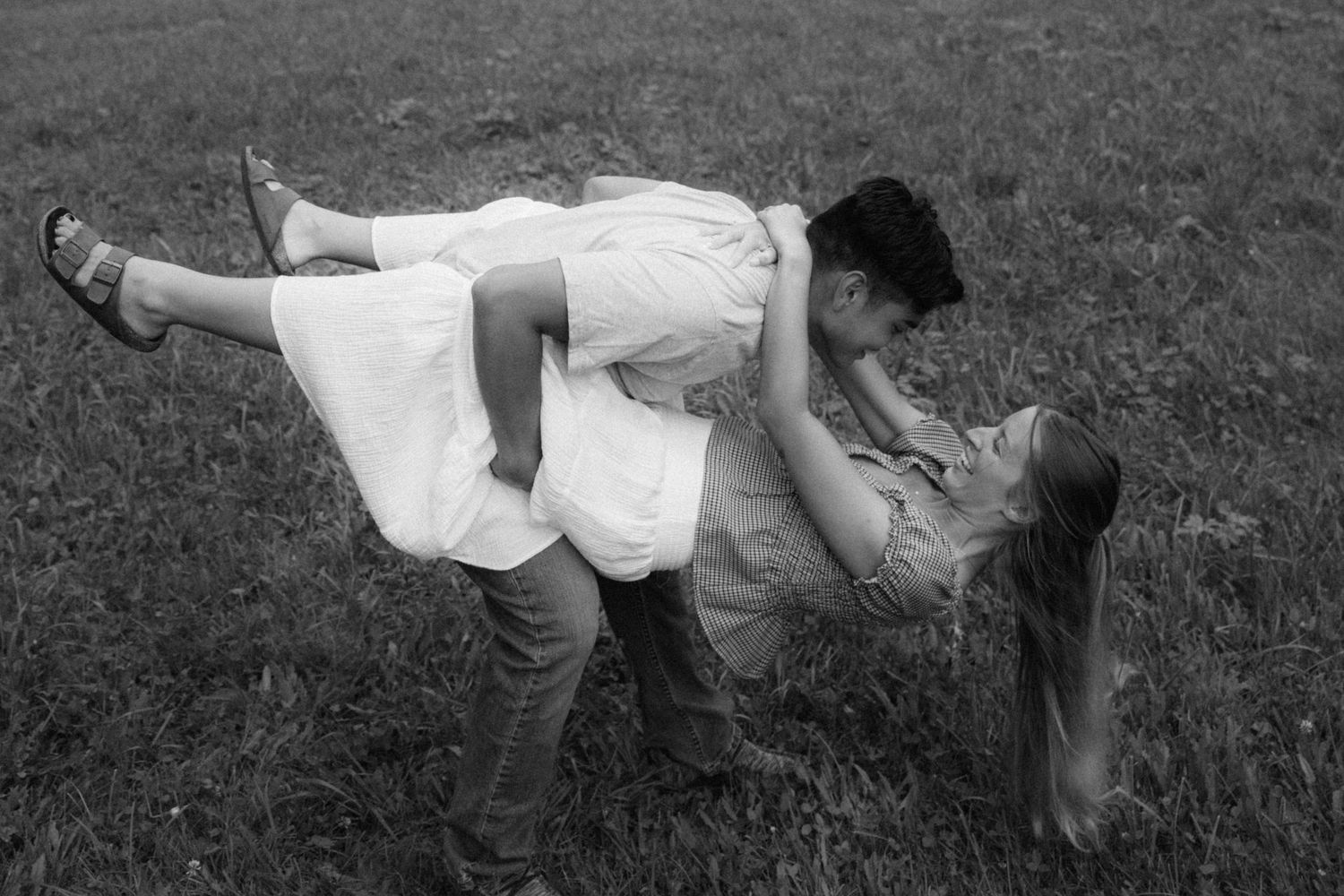 Seven black and white wedding photos show romantic moments of newlyweds dancing and embracing in a grassy field.