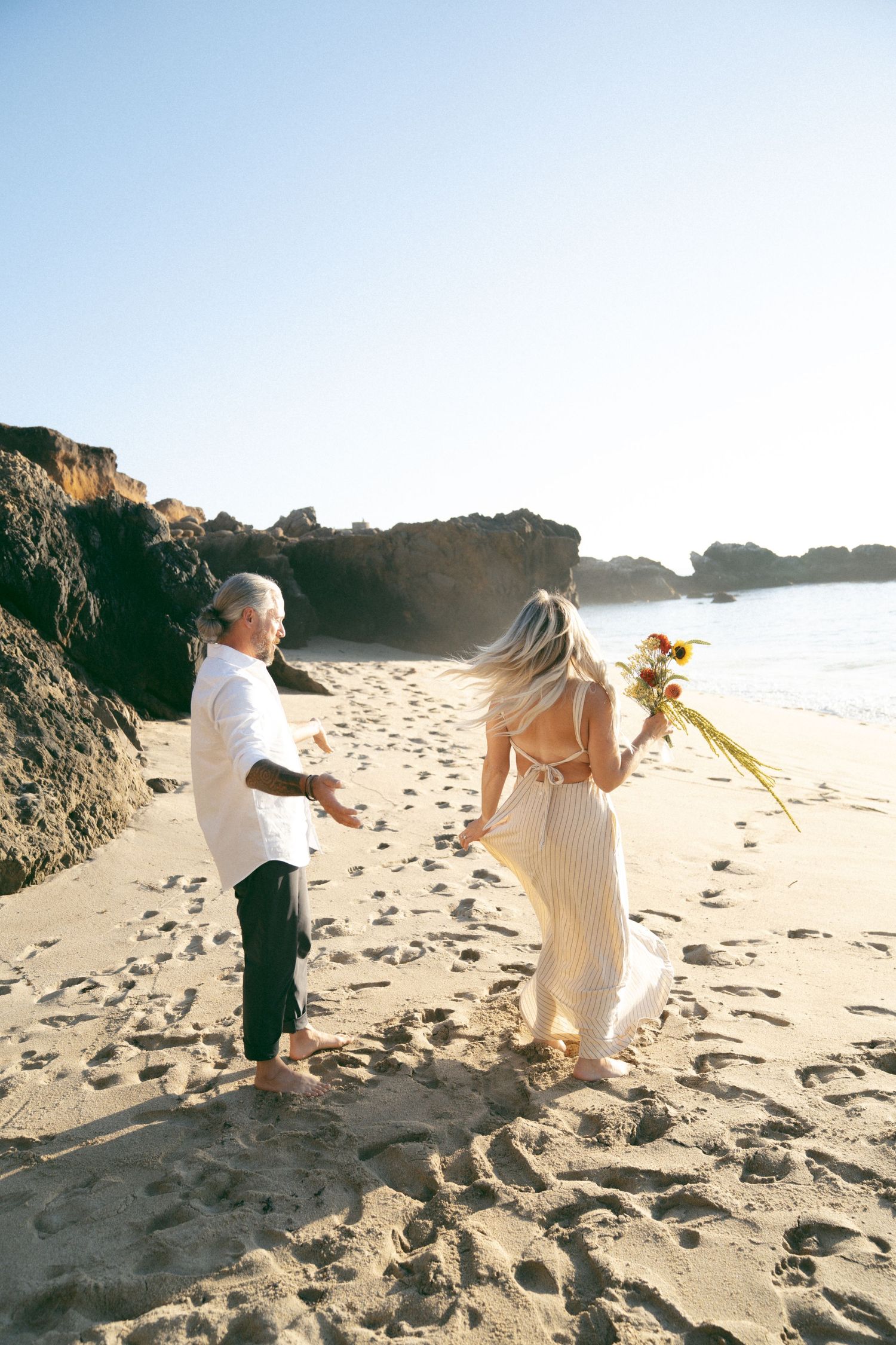 Two children play together on a sunlit sandy beach with cliffs visible in the background.