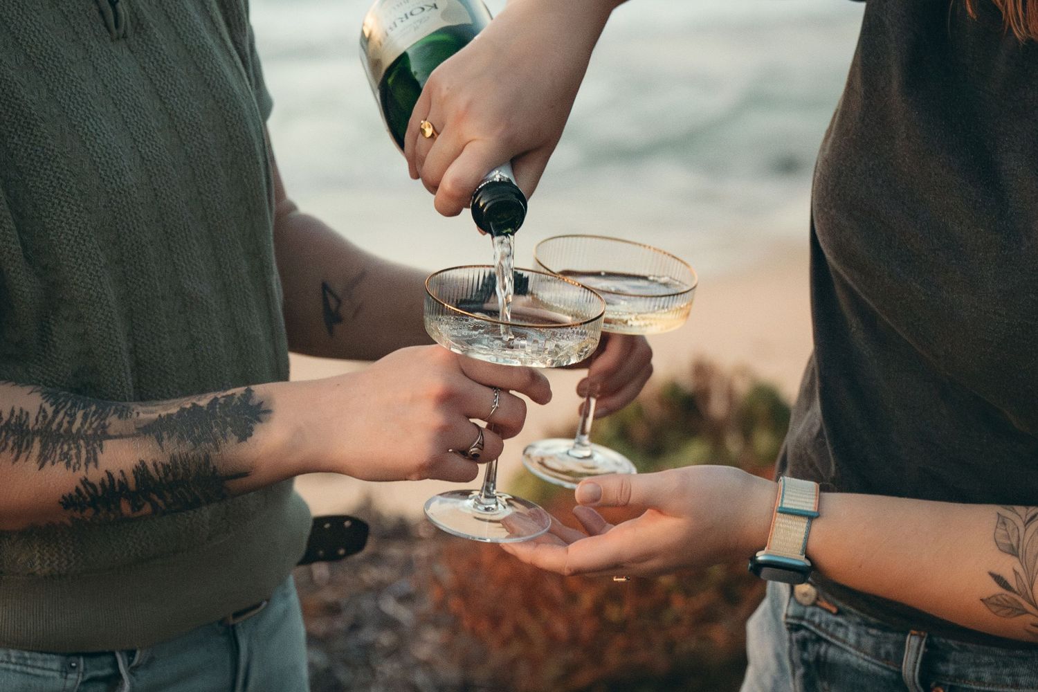 Close-up view of hands holding martini glasses with cocktails during a social gathering outdoors.