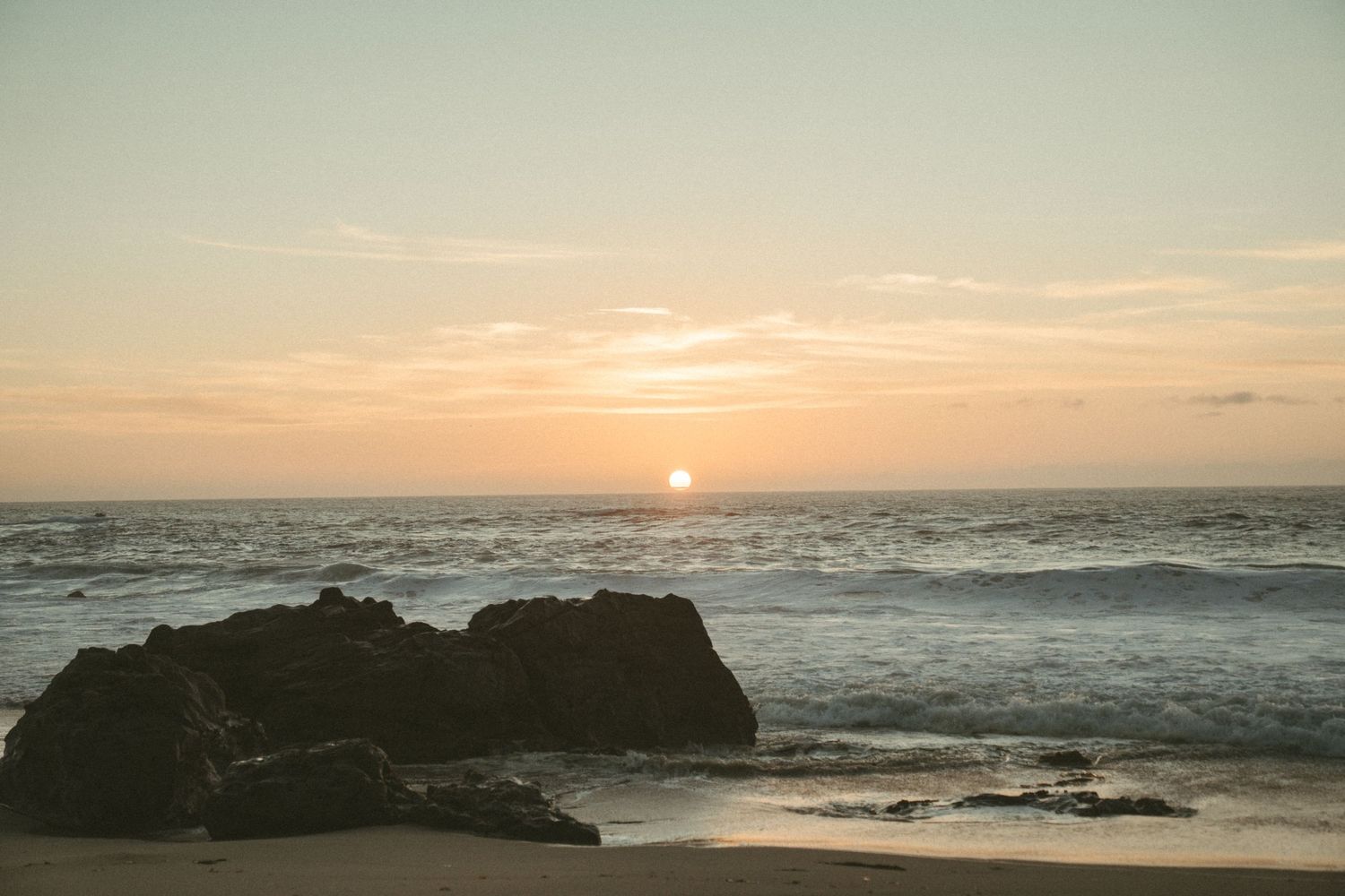 Stunning sunset over the ocean horizon with waves crashing against rocky coastline during golden hour.