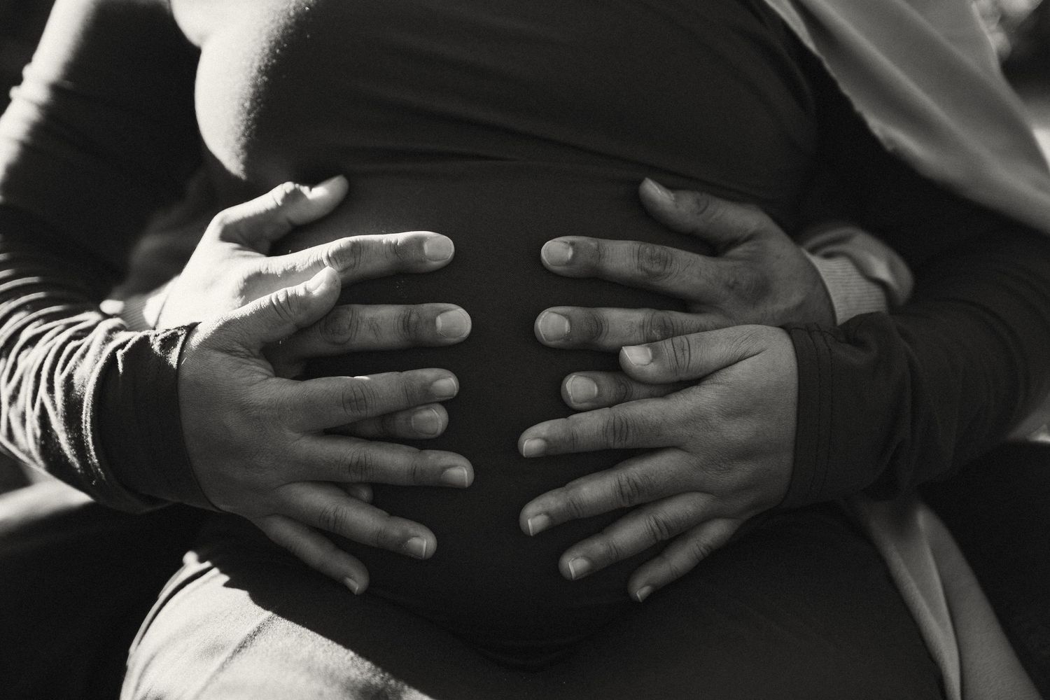 Black and white close-up of hands gently resting on a pregnant belly during a maternity photoshoot.