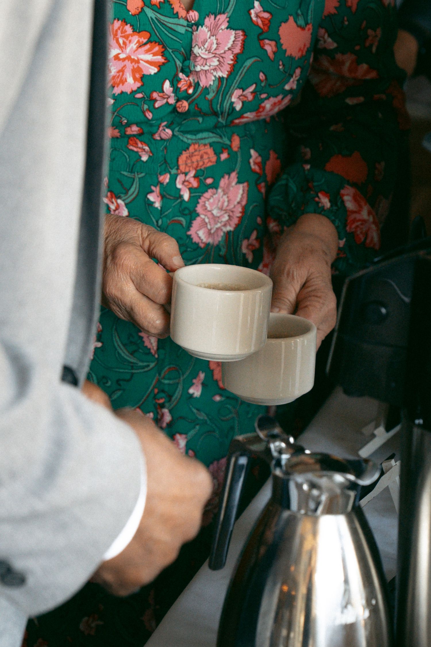 Hands hold and adjust a white coffee filter holder over a glass carafe while brewing coffee.