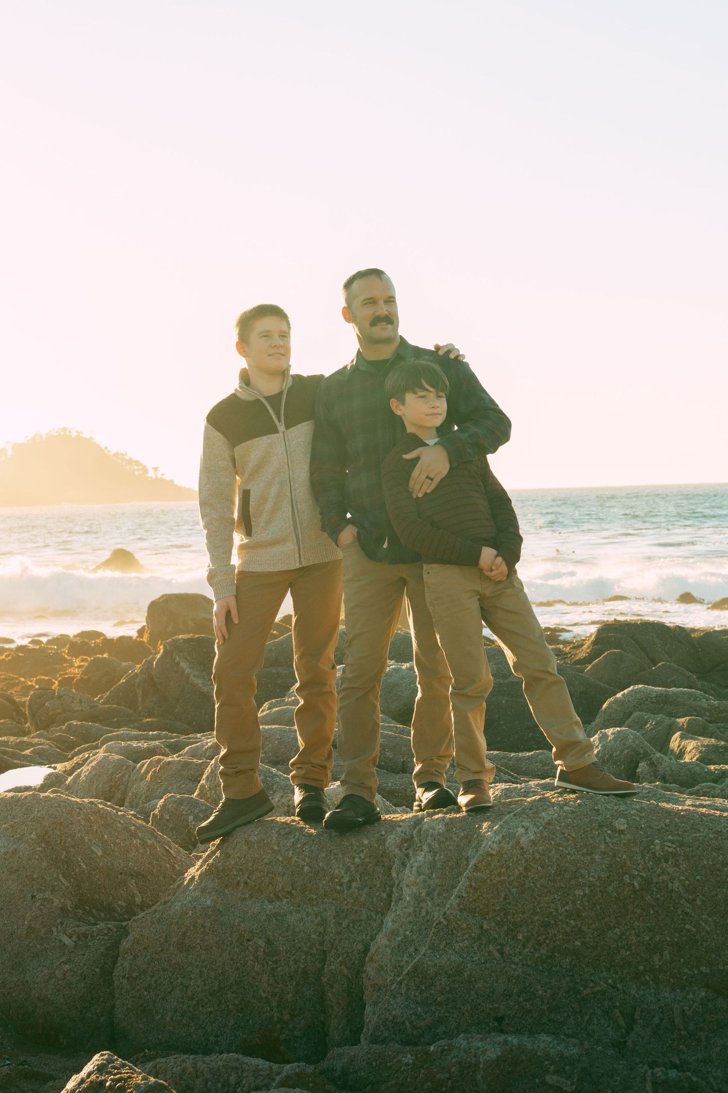 Group gathered on rugged ocean rocks during sunset with waves crashing in background.
