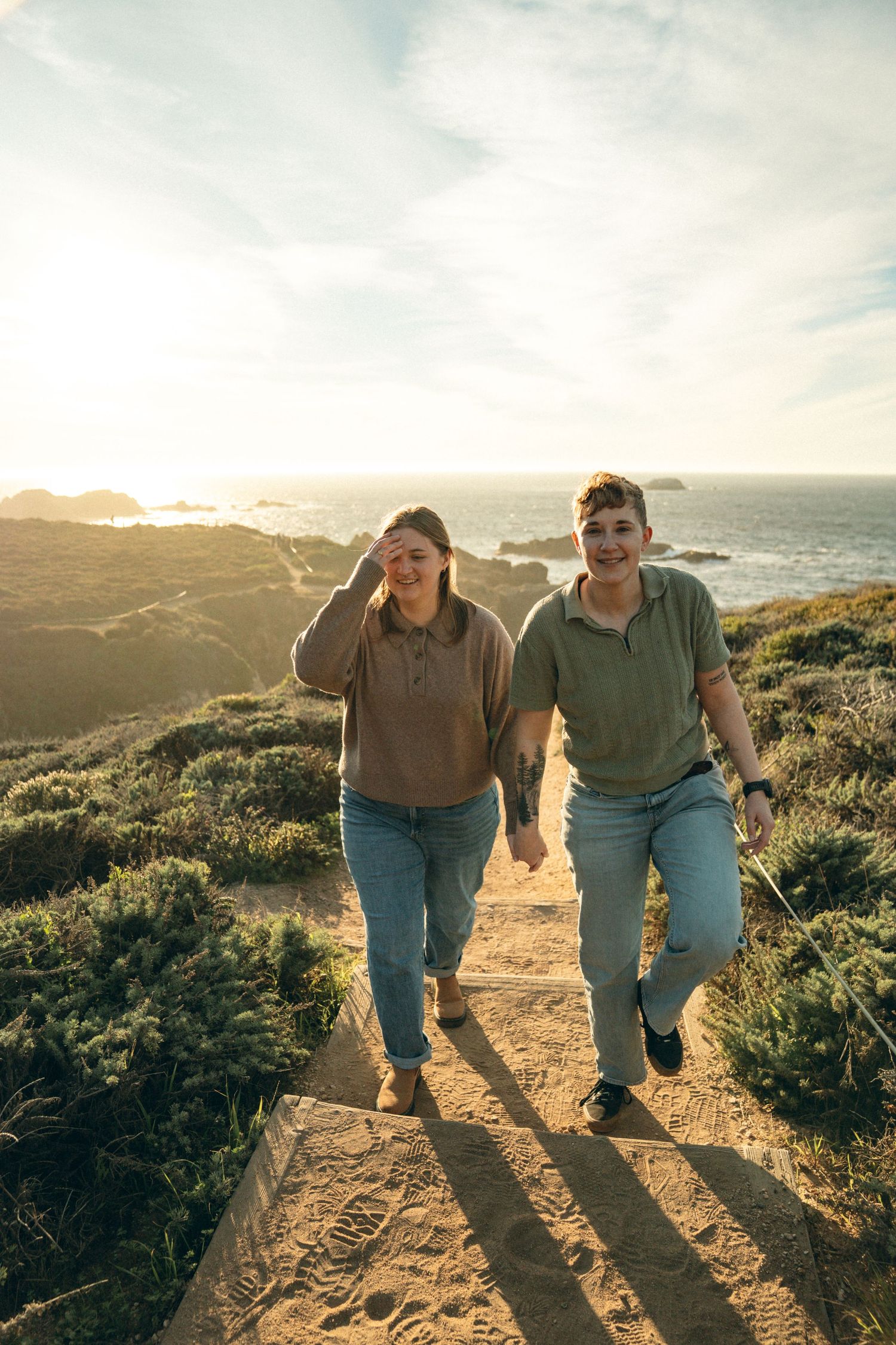 Two people walking together on coastal trail during golden hour casting long shadows.