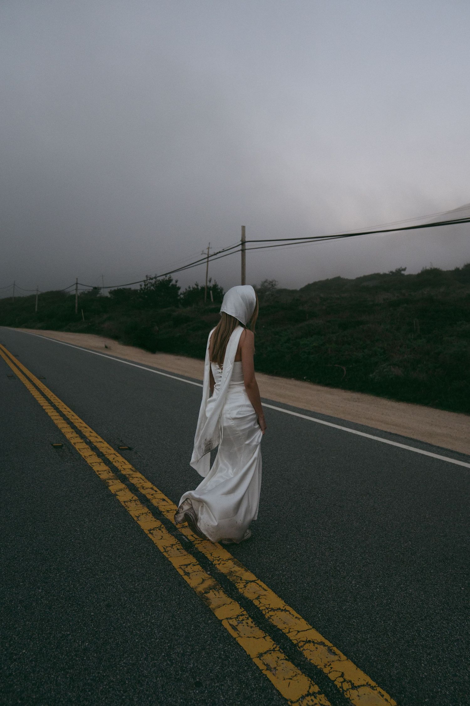 A series of atmospheric shots showing a figure in white moving along a foggy mountain road with yellow lines.