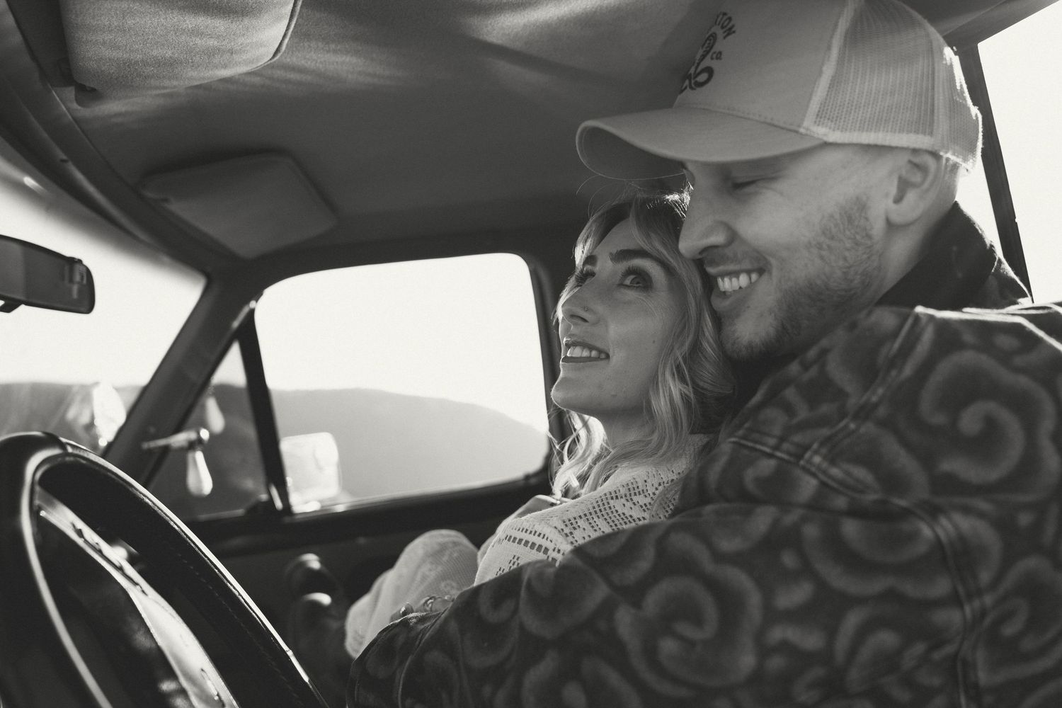 Happy couple sharing romantic moment together in vintage car in black and white photo.