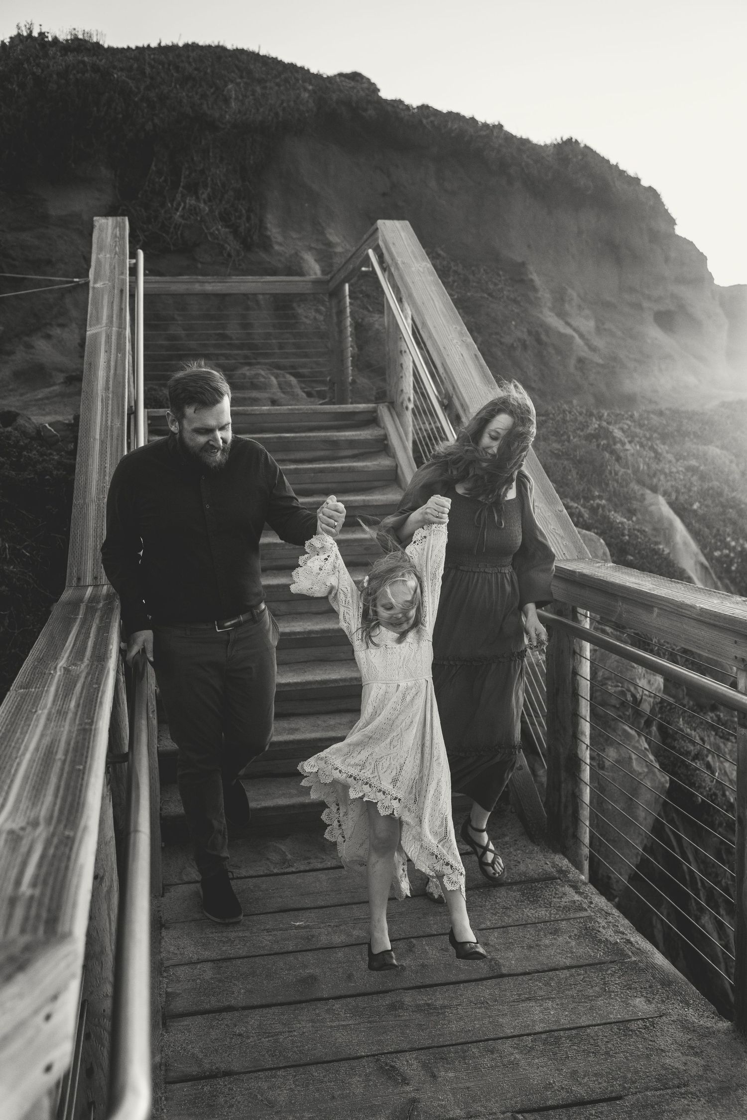 Family playing and dancing together on wooden steps overlooking a scenic coastal view at golden hour.