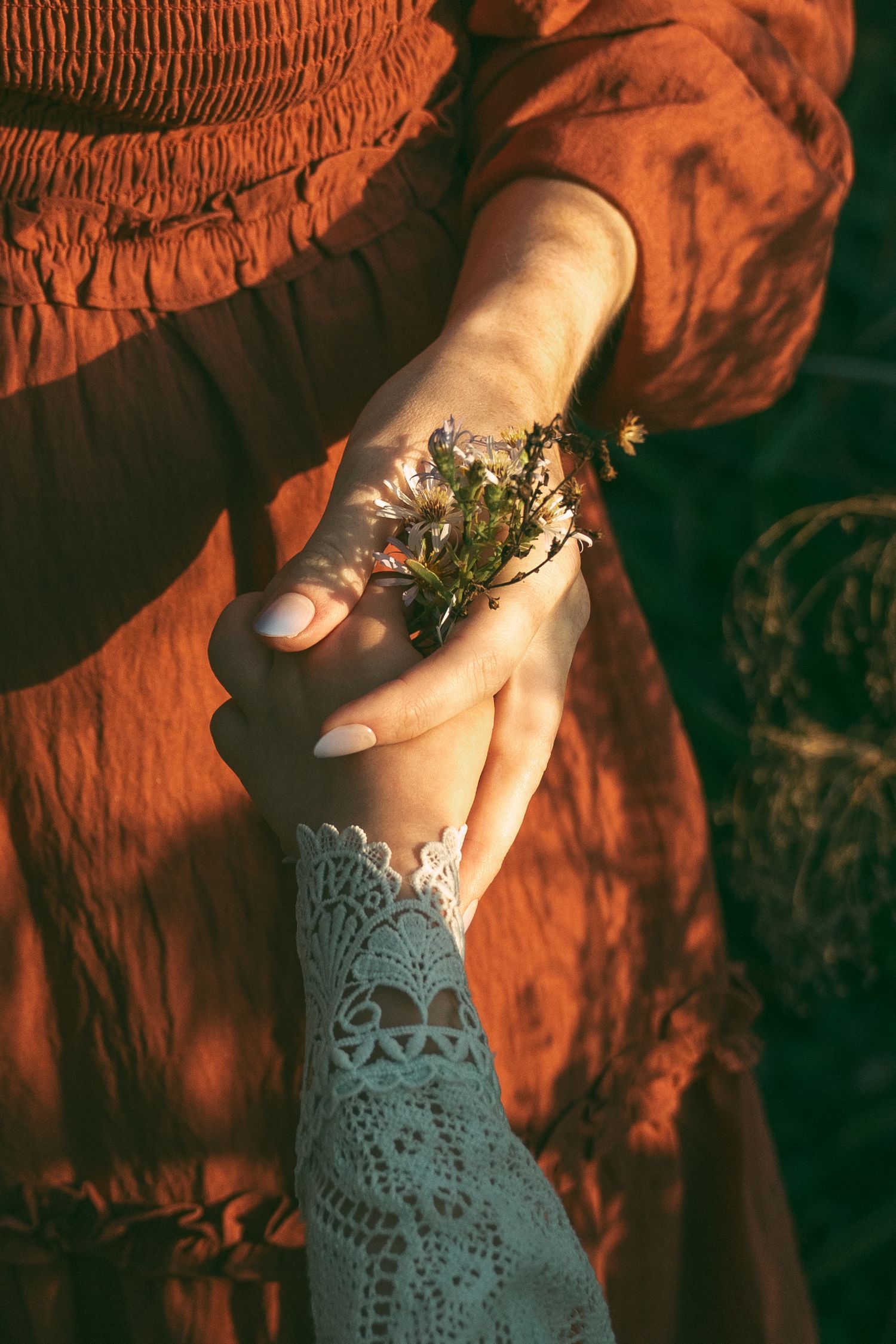 Hand wearing a white lace glove holds a small delicate butterfly in warm sunlight against an orange backdrop.