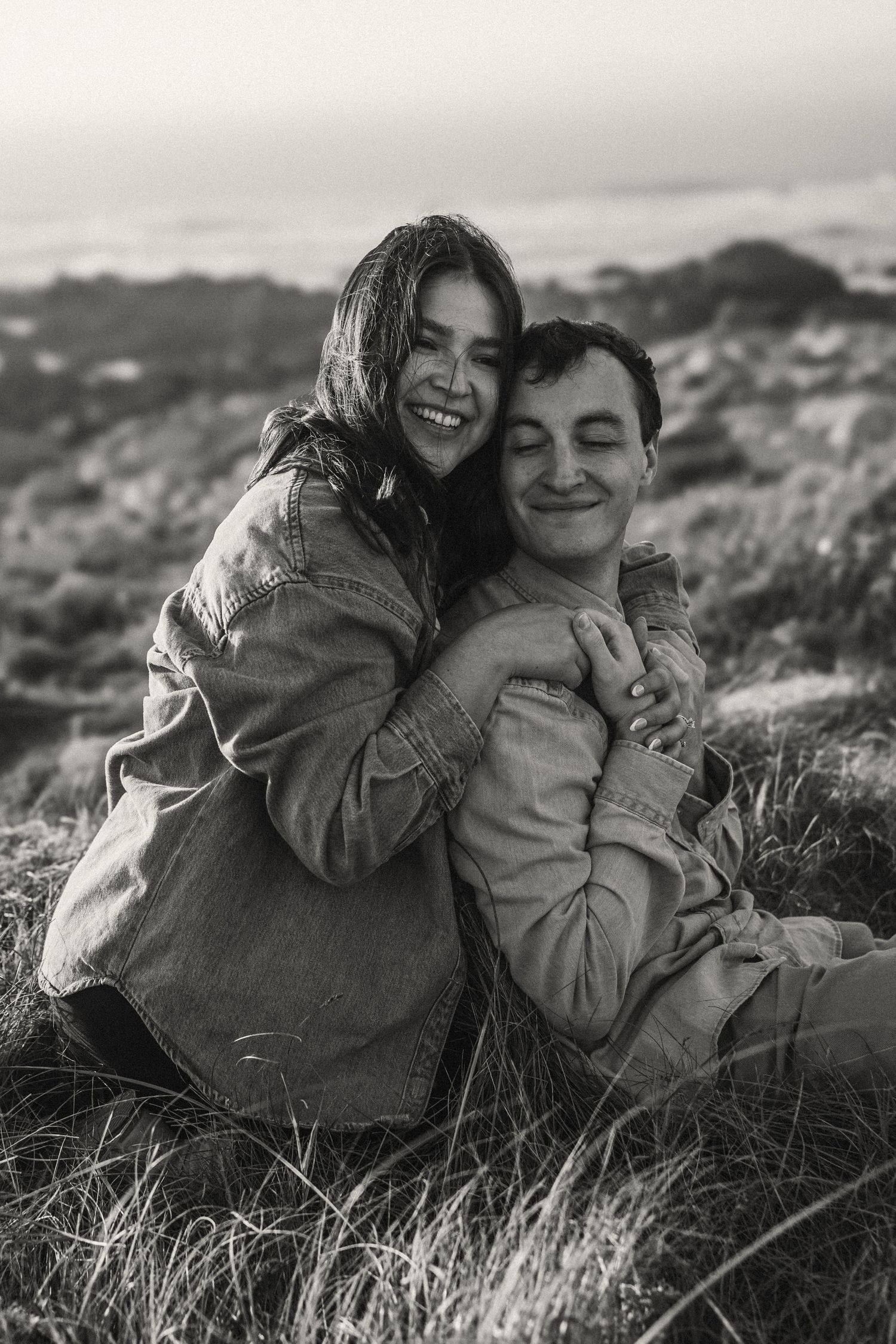 A candid black and white photo of a couple embracing and laughing outdoors.