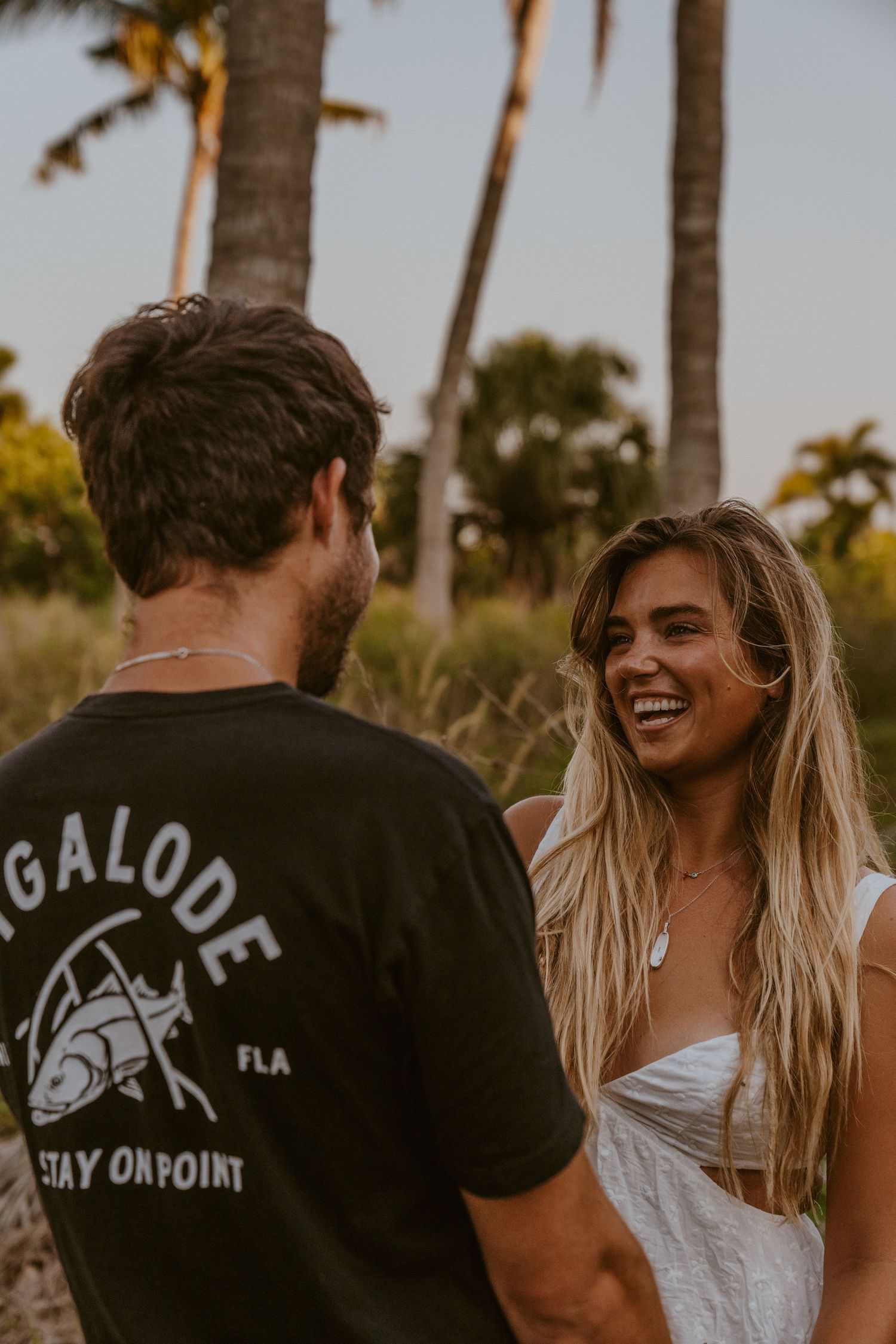 A couple sharing a joyful moment together among palm trees during golden hour in Florida.